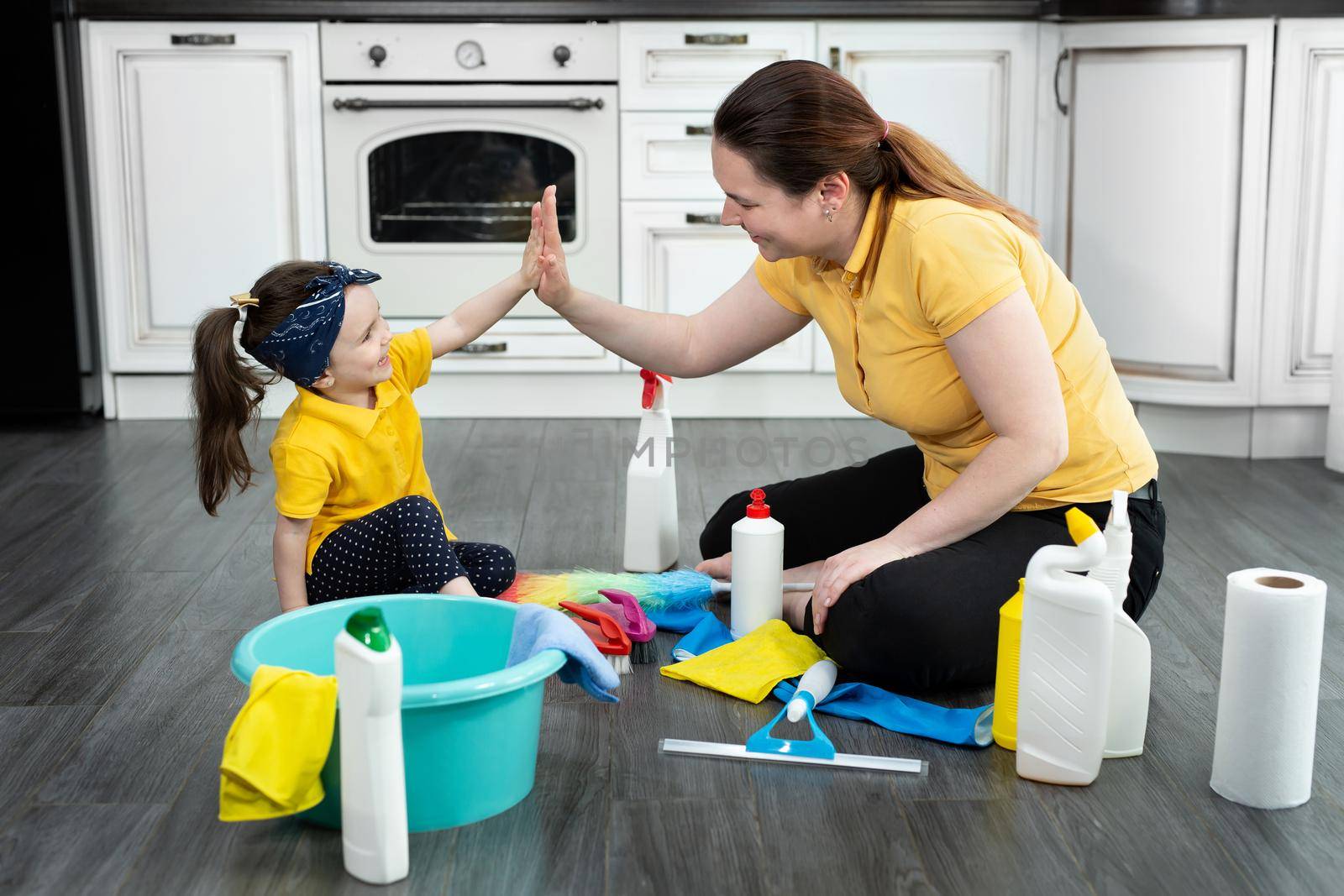 Beautiful young woman and her little daughter sit on the floor and have fun cleaning their house