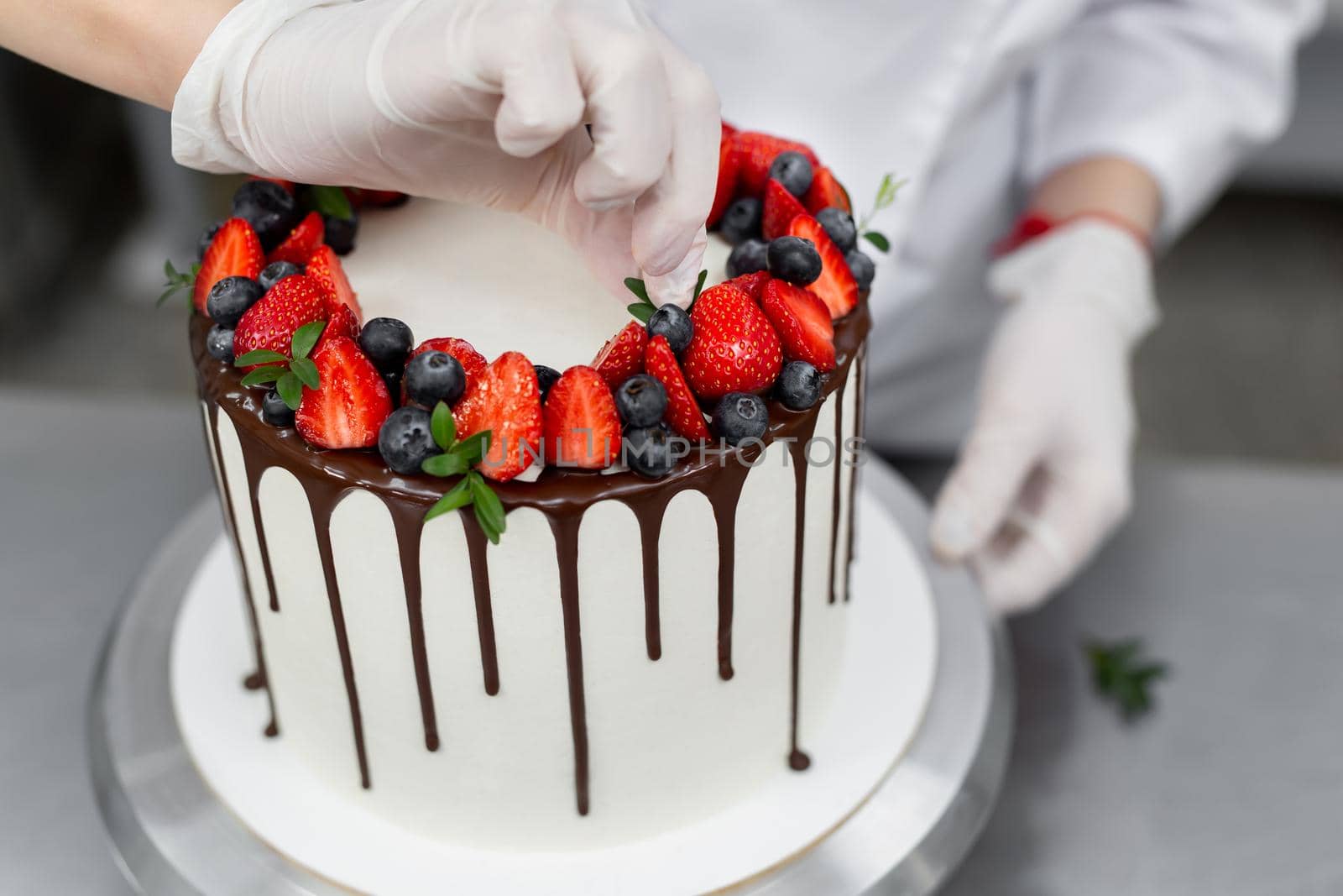 Pastry chef decorates the cake with chocolate levels of berries and mint by StudioPeace