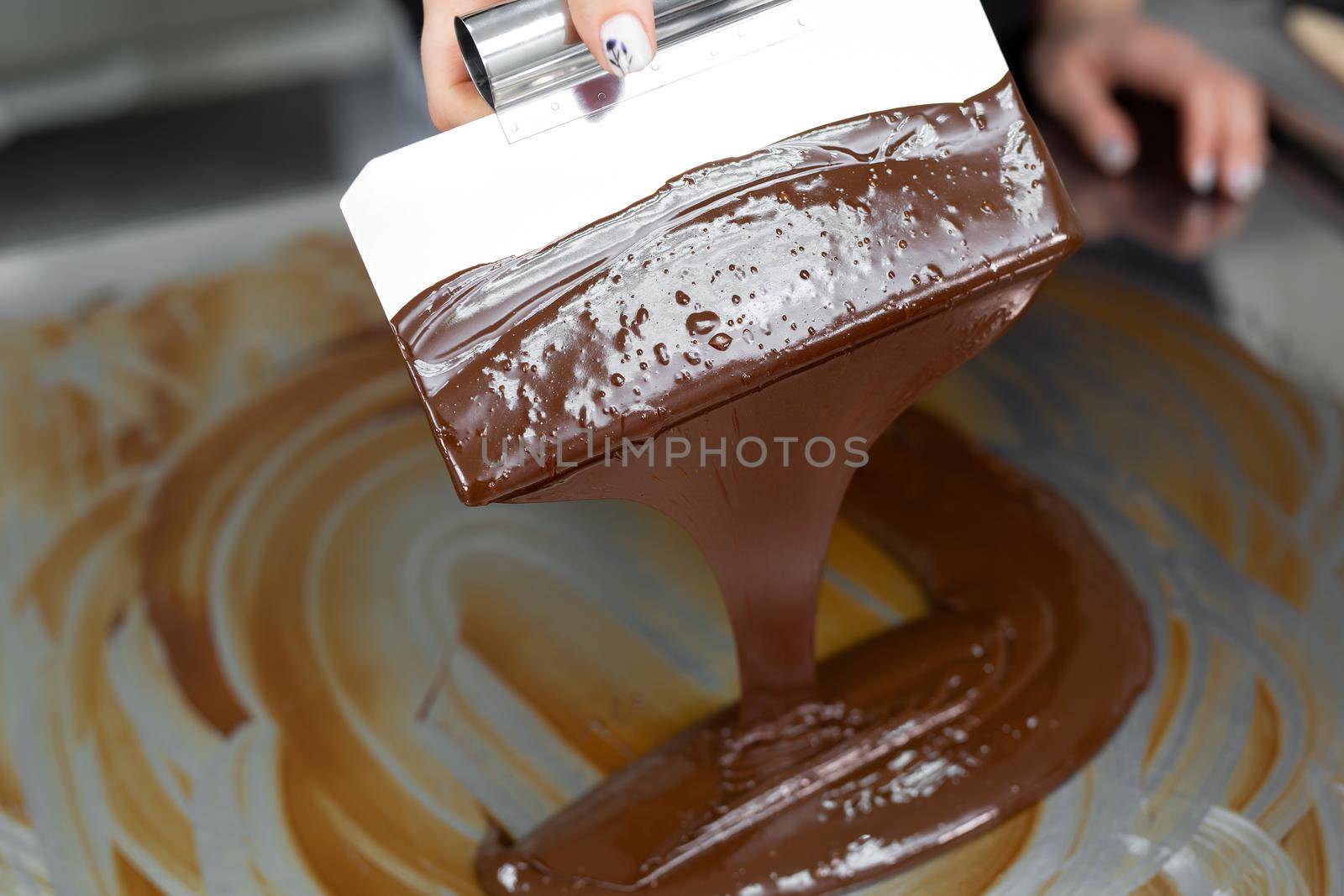 Close-up of a pastry chef using spatulas tempering molten chocolate. by StudioPeace