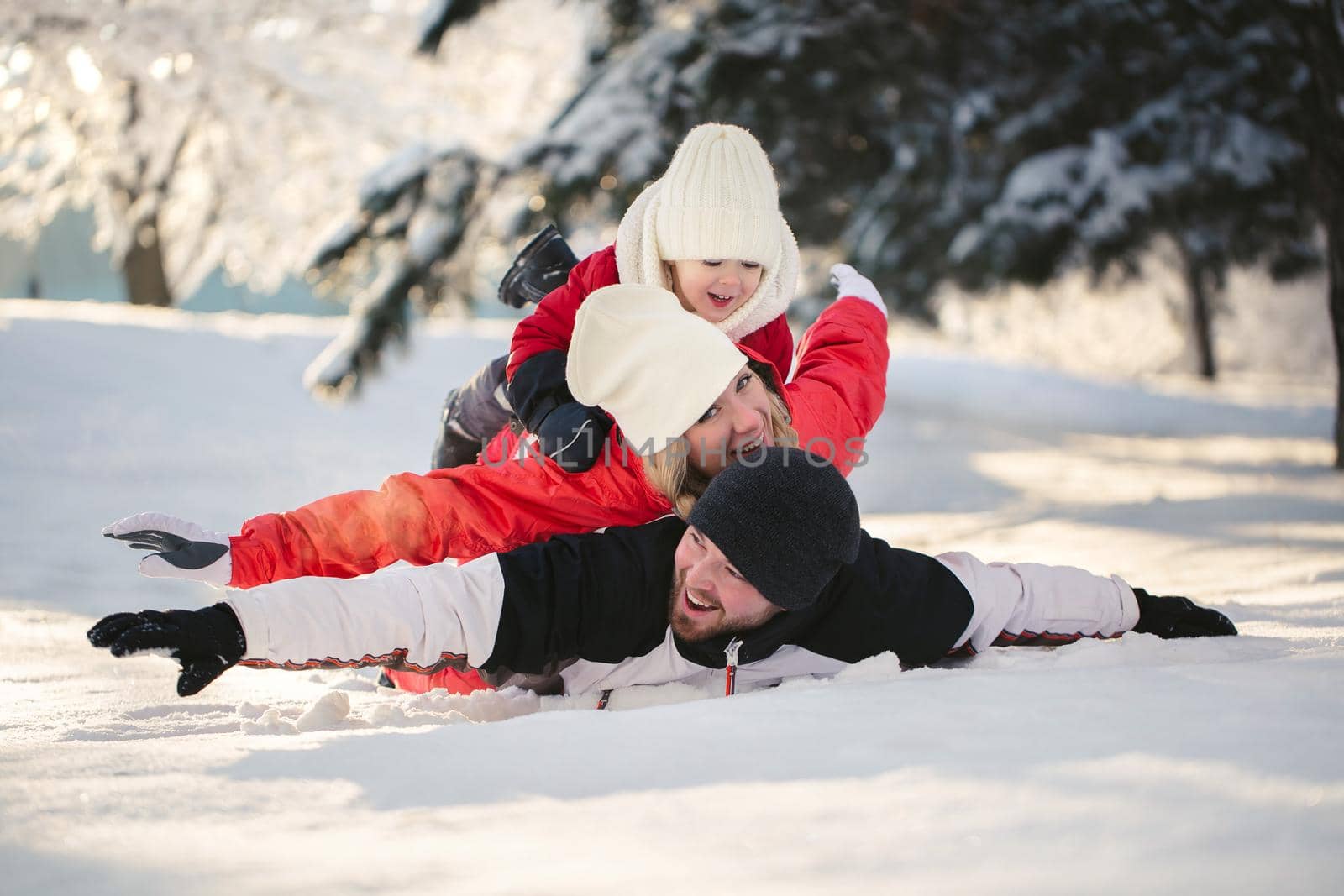 Cheerful parents and son are lying in the snow in the winter in the forest by StudioPeace