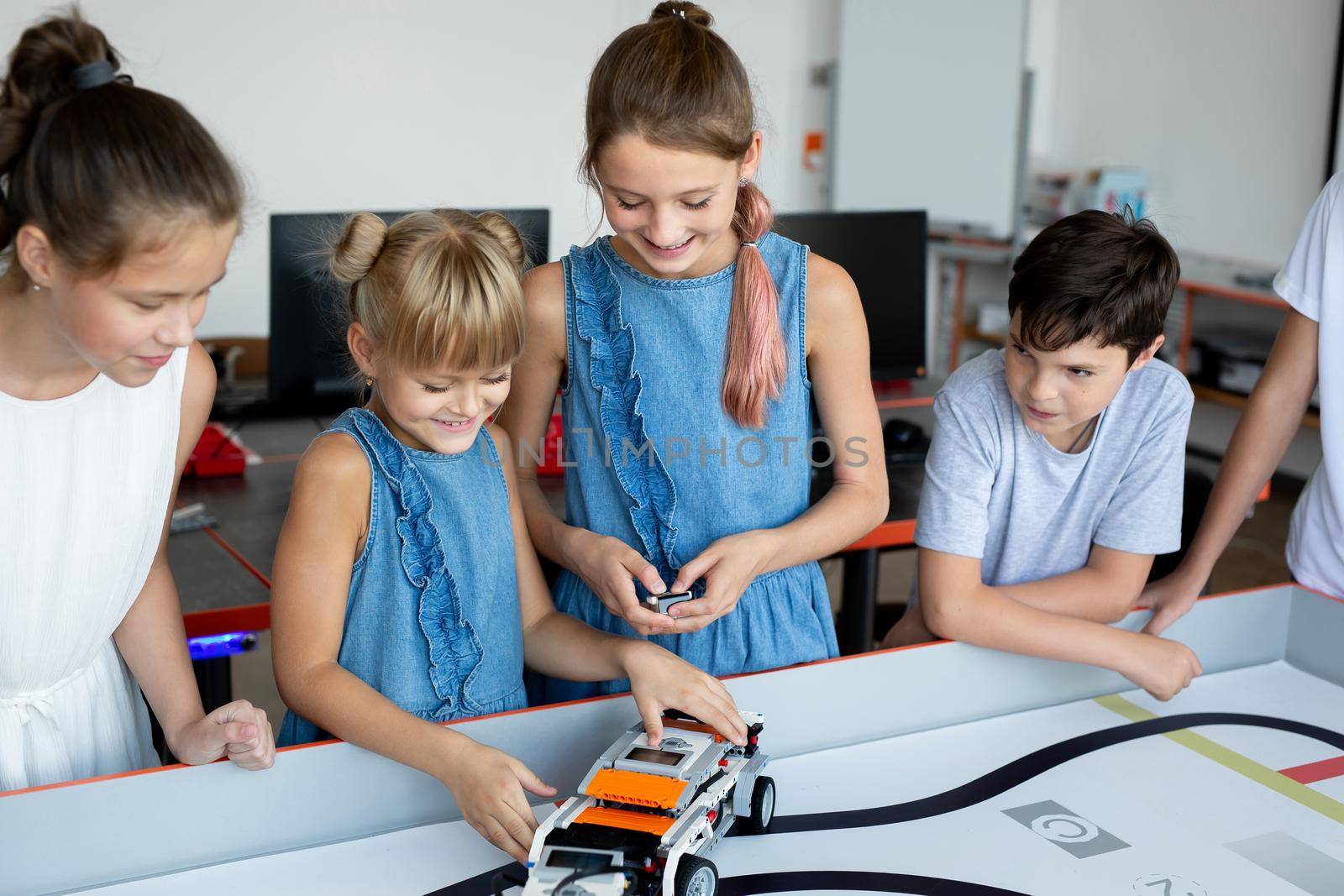 Portrait of happy children at school in the office at a robotics lesson, with a modern office with computers in the background. by StudioPeace