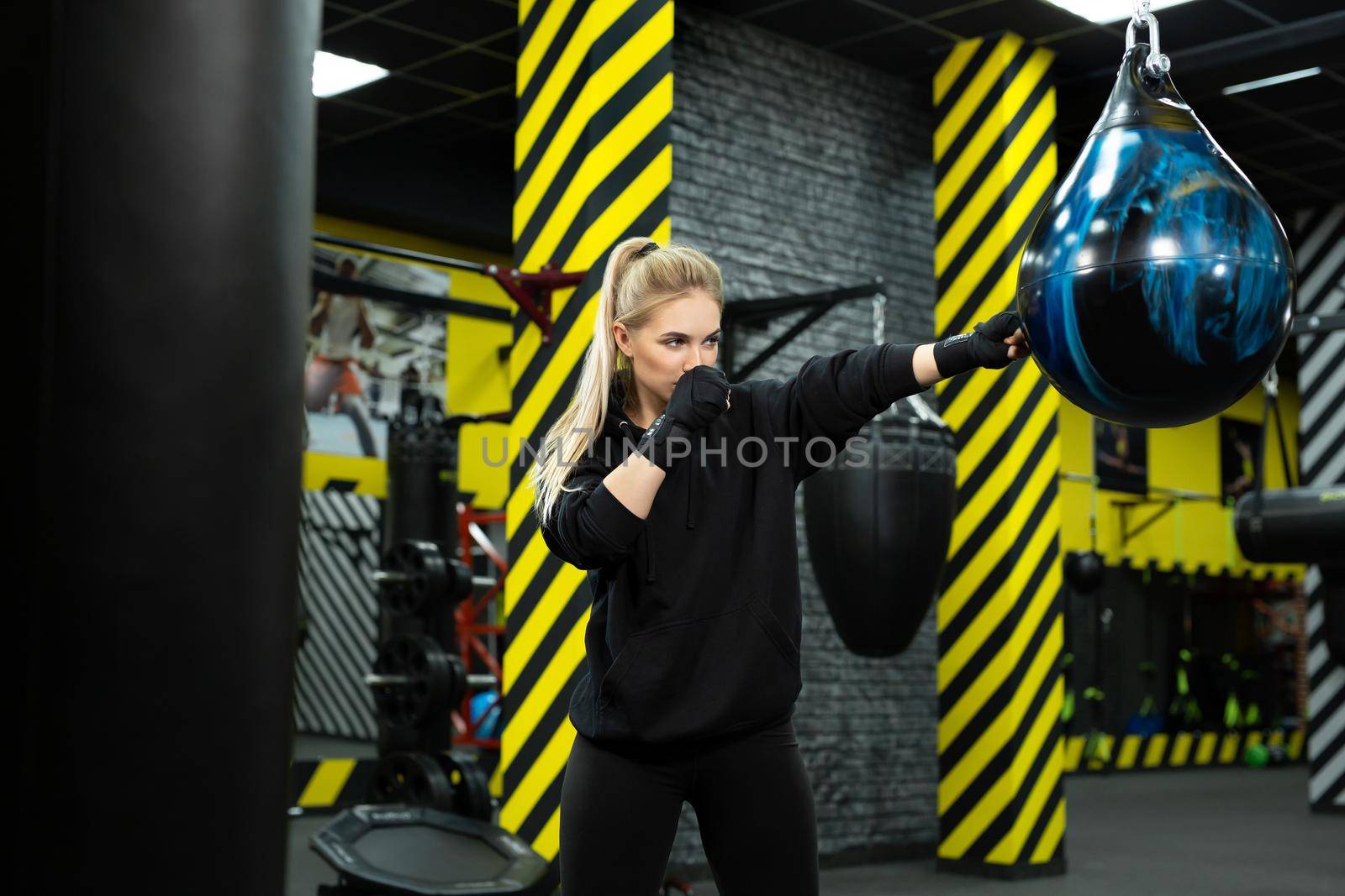 Young female athlete in blue boxing gloves hits a pear in the ring.