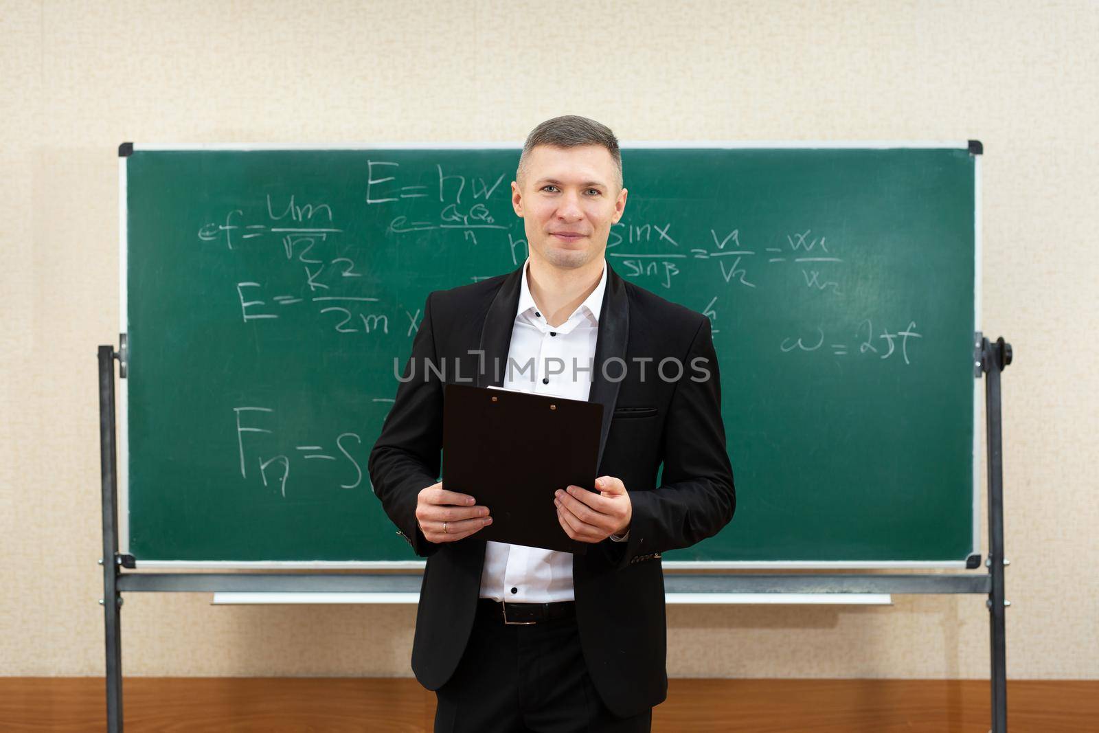 The male teacher used white chalk to write on the blackboard to teach students in a class by StudioPeace