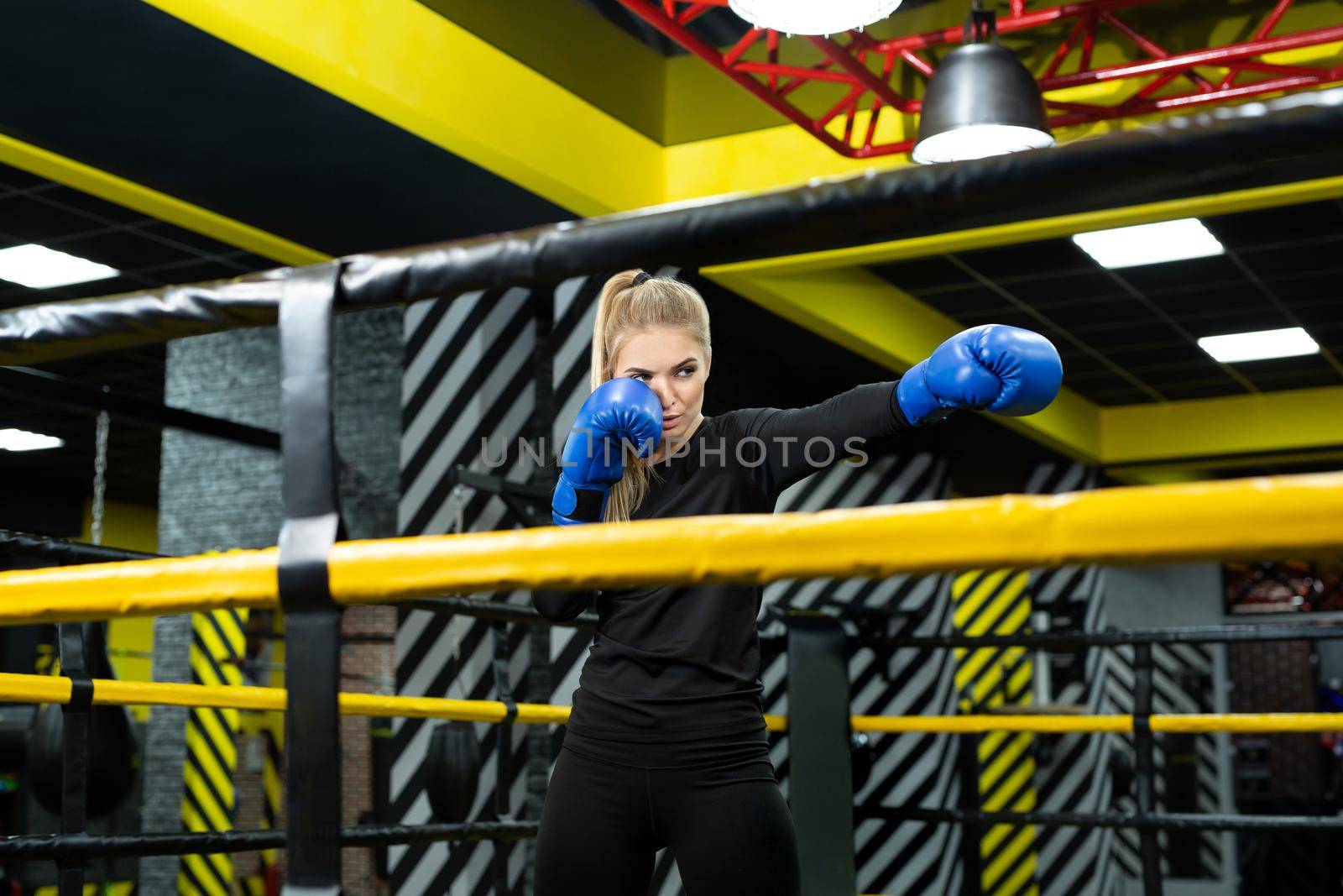 Young female athlete in blue boxing gloves hits a pear in the ring.