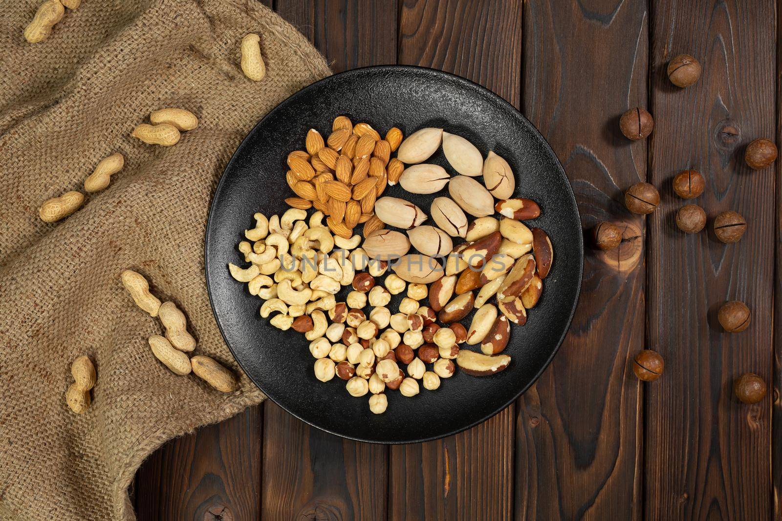 Mixture of nuts in a black plate on a brown wooden background.
