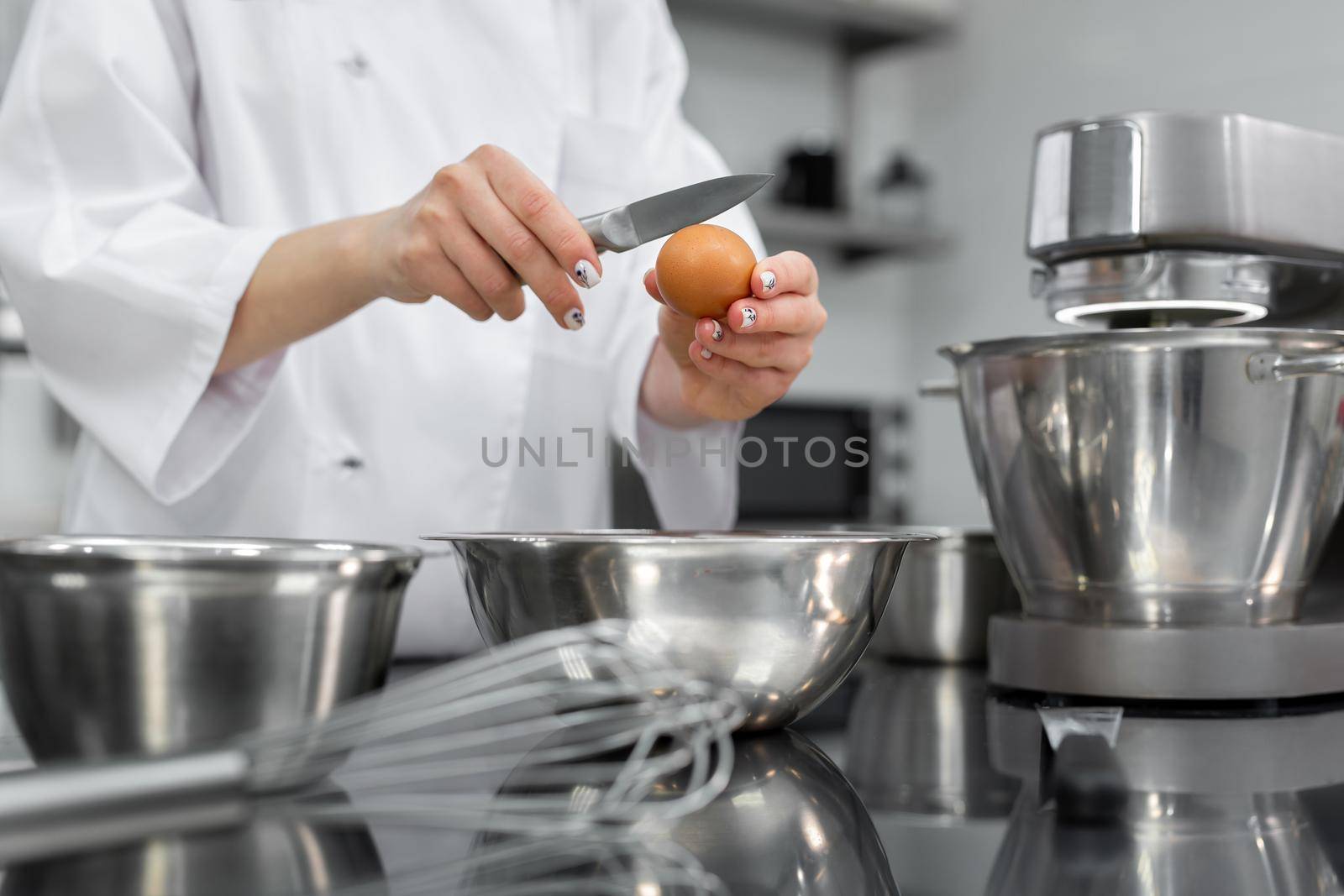Hands of a pastry chef break an egg with a knife in a professional kitchen.