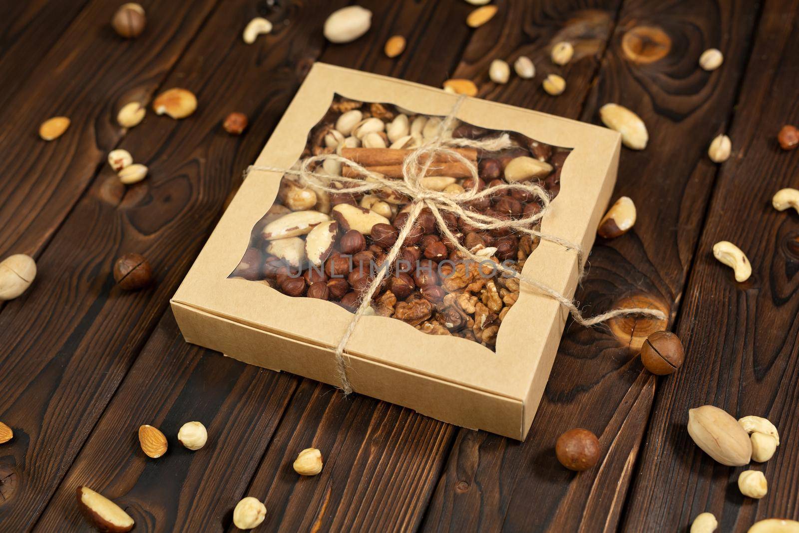 Nuts of different varieties in a box on a structural wooden background top view. Assorted nuts in a paper box.