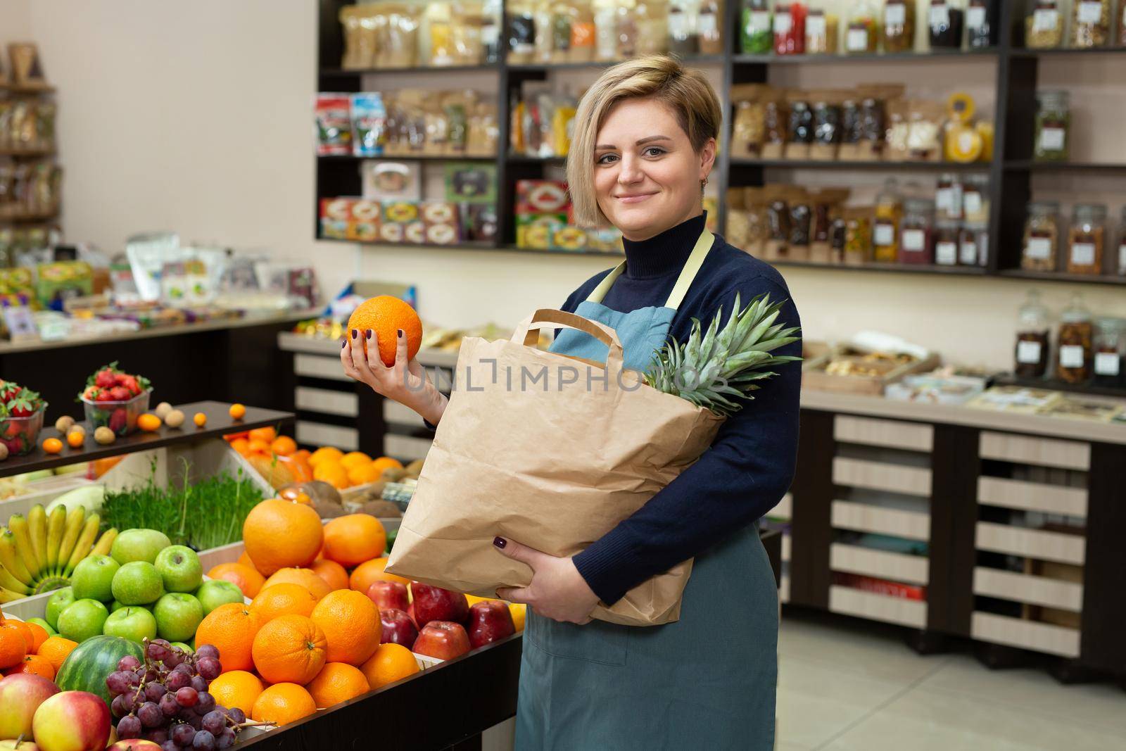 Young saleswoman collects vegetables and fruits in a paper bag by StudioPeace