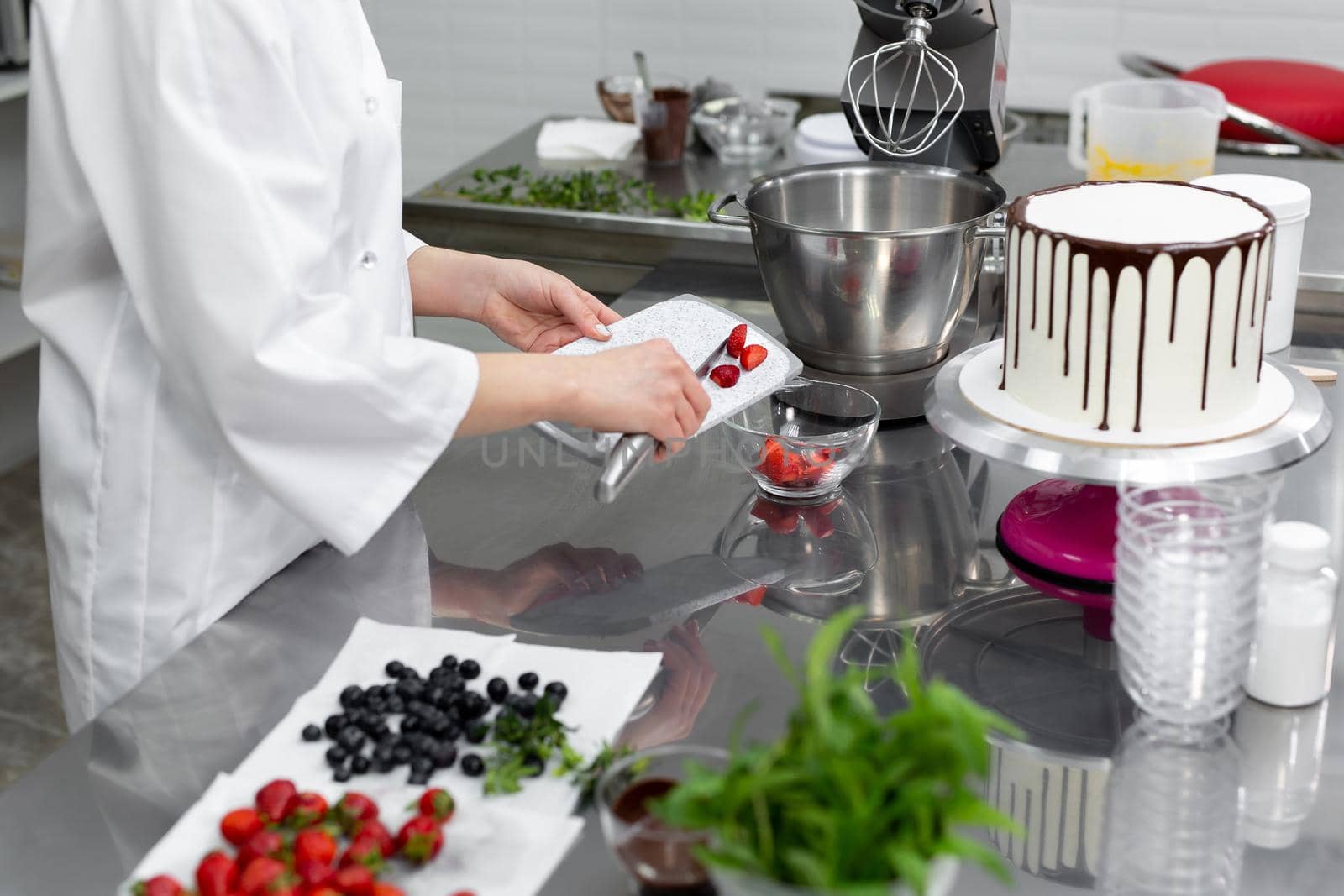 Pastry chef cuts strawberries to decorate the cake. by StudioPeace