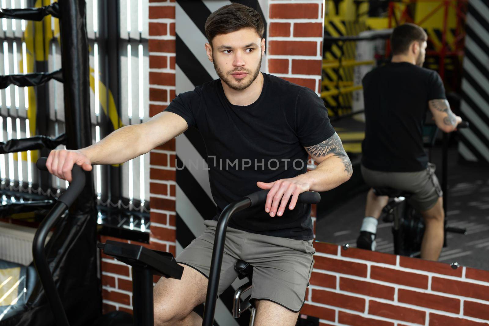 Young athletic male boxer trains on an exercise bike near the ring by StudioPeace