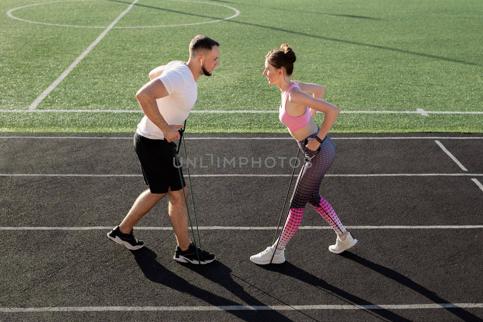 Young fitness couple trains at the stadium in the summer with an elastic expander. by StudioPeace