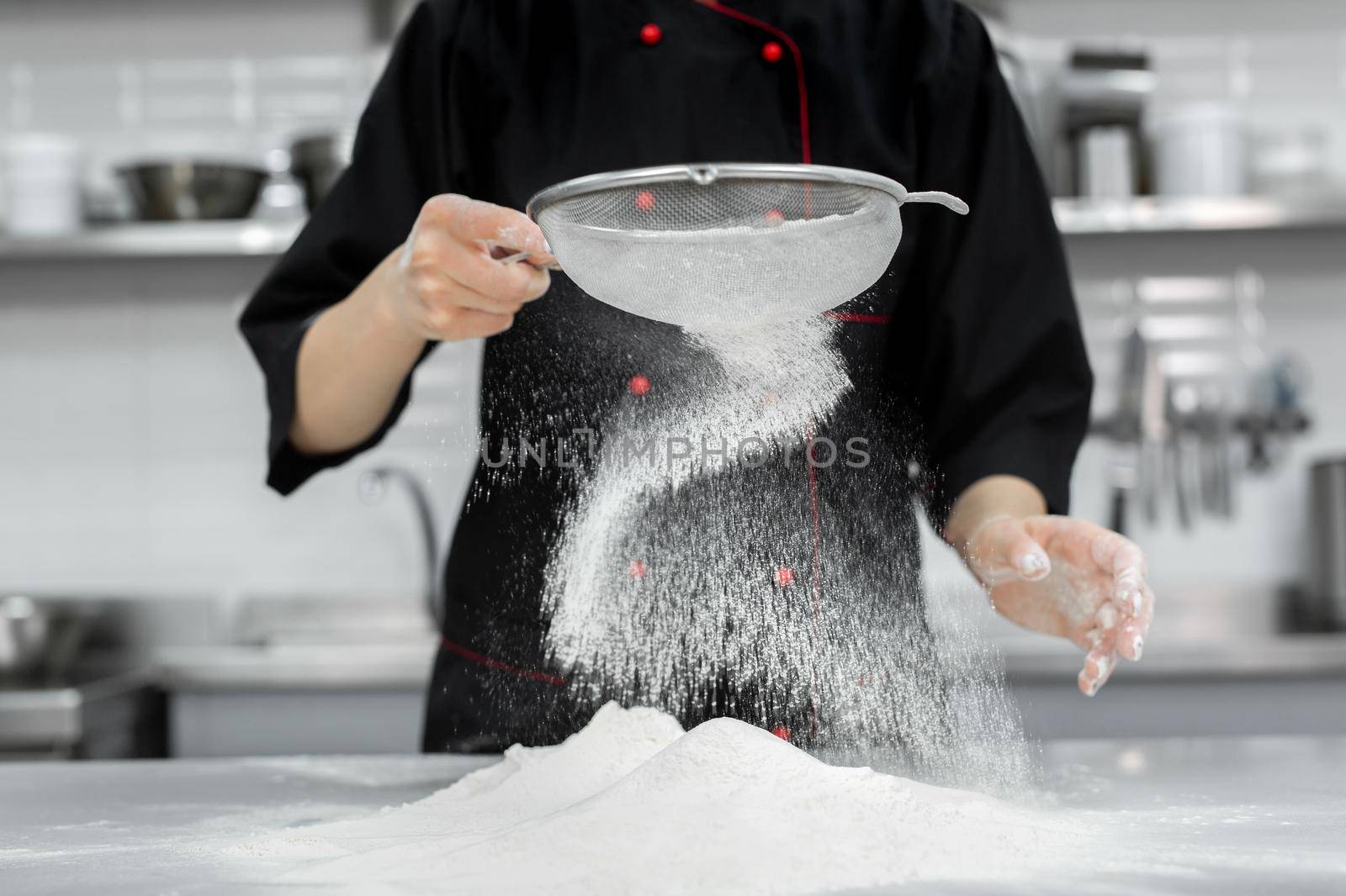The pastry chef's hands sift the flour through a sieve on the table.