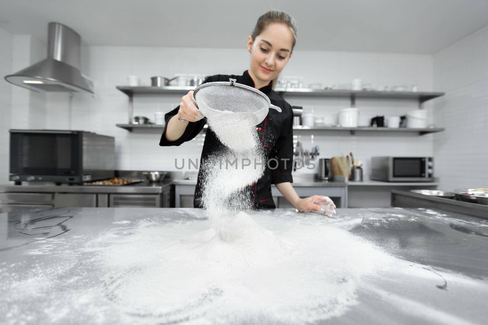The pastry chef sows the flour through a sieve on the table by StudioPeace