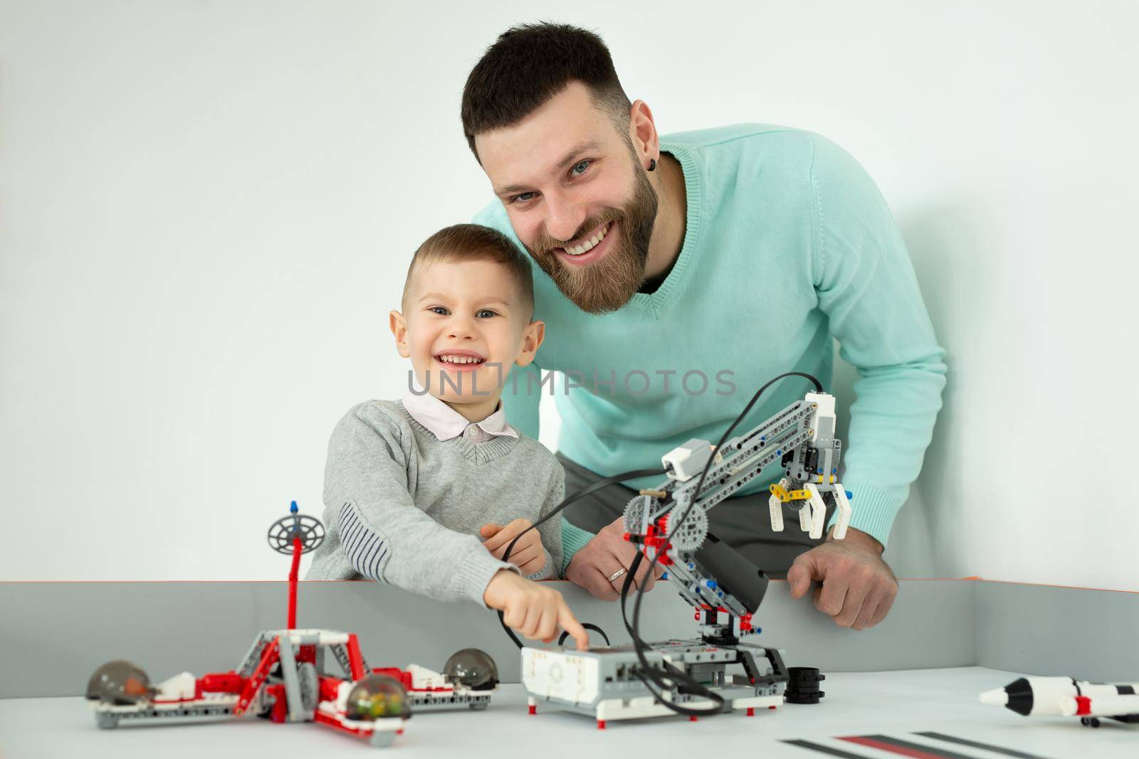 Happy handsome man smiling to the camera with his cheerful young son while playing with cars together robots activity weekend