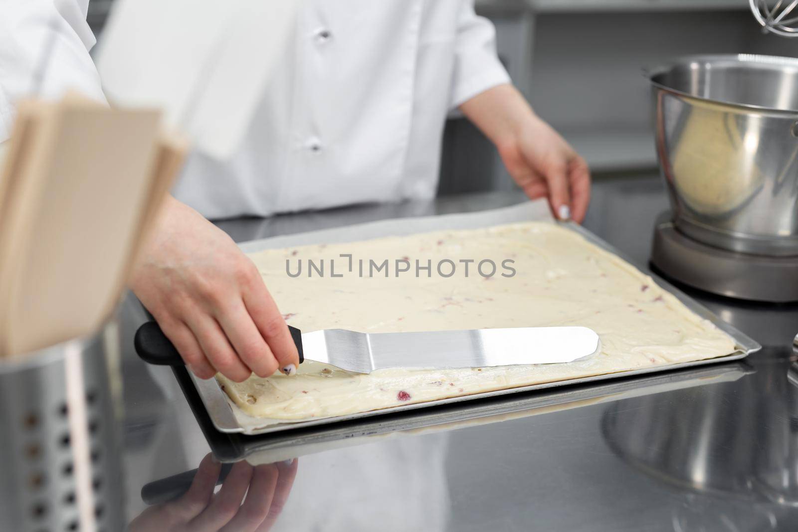 Pastry chef levels the biscuit on parchment before baking by StudioPeace