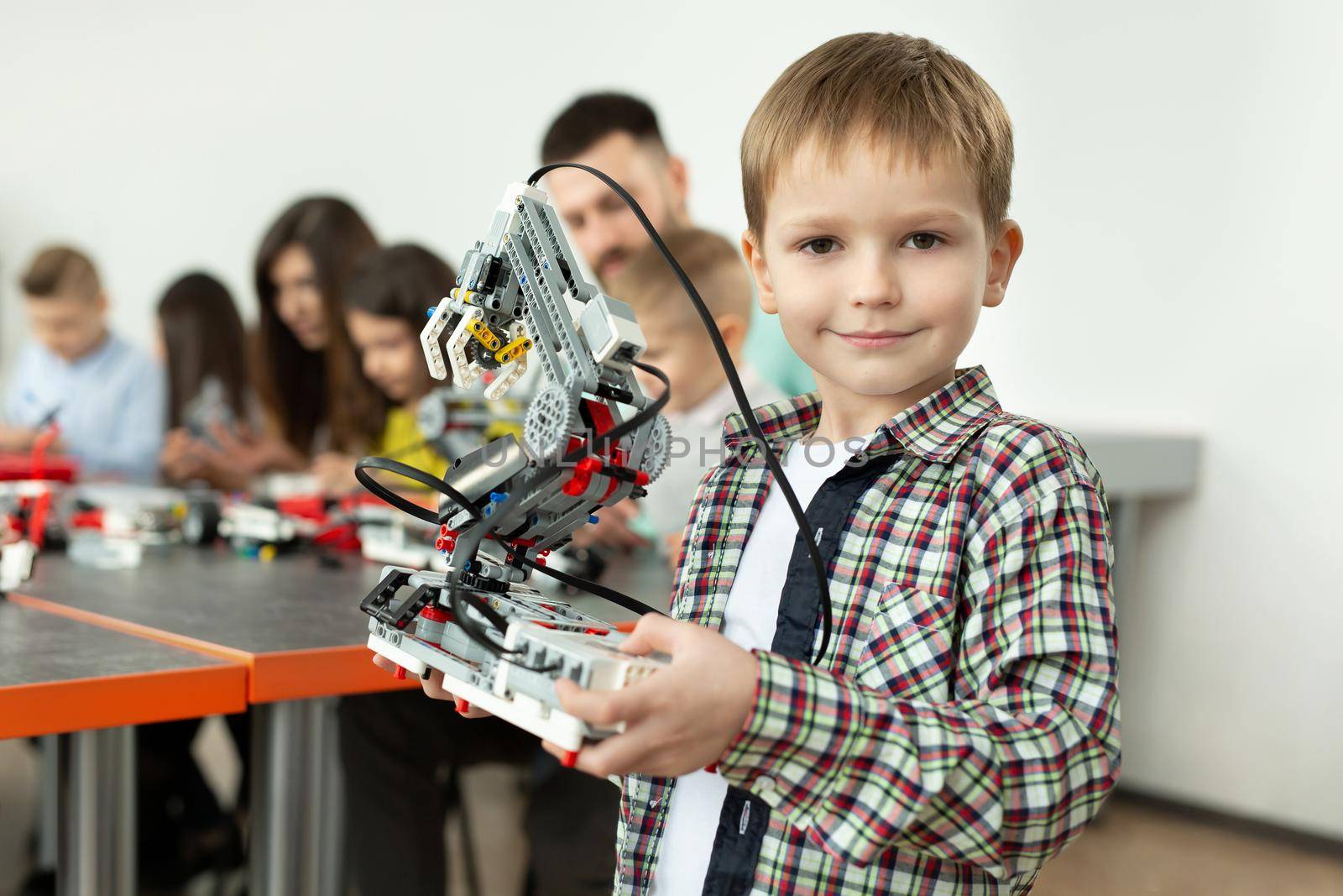 Portrait of a smart boy in a robotics class at school, holding a robot that he assembled from plastic parts programmed on a computer by StudioPeace