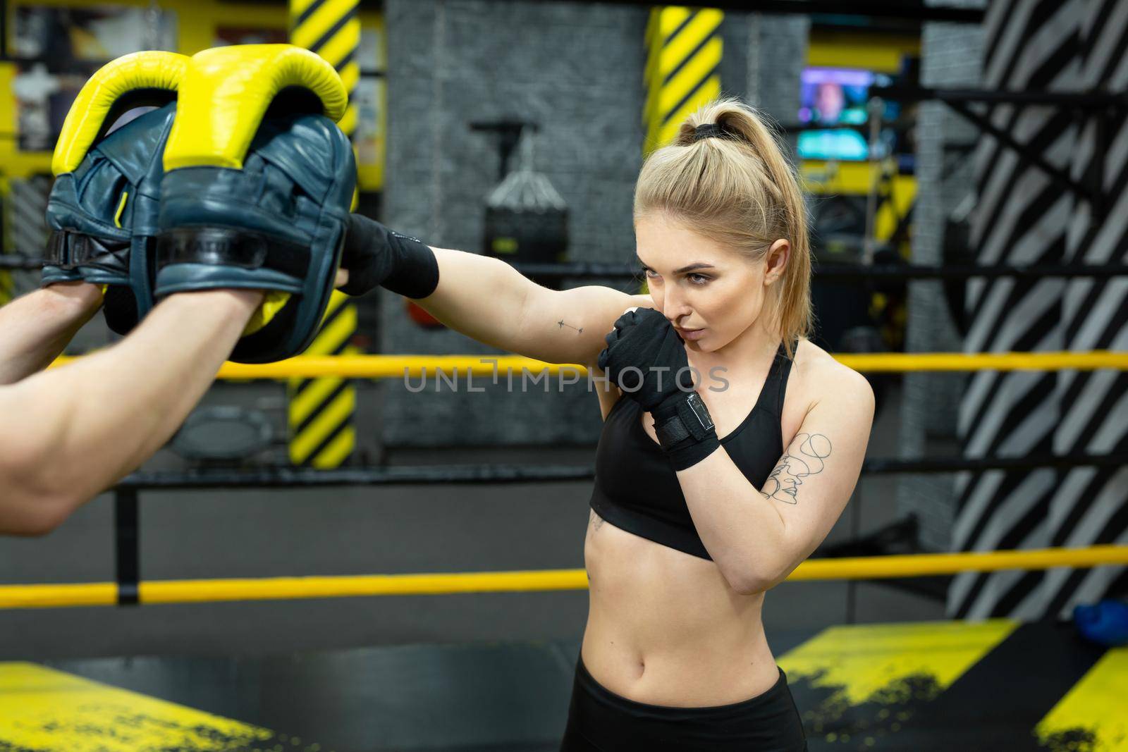 Beautiful girl in boxing gloves hits the paws held by her trainer.