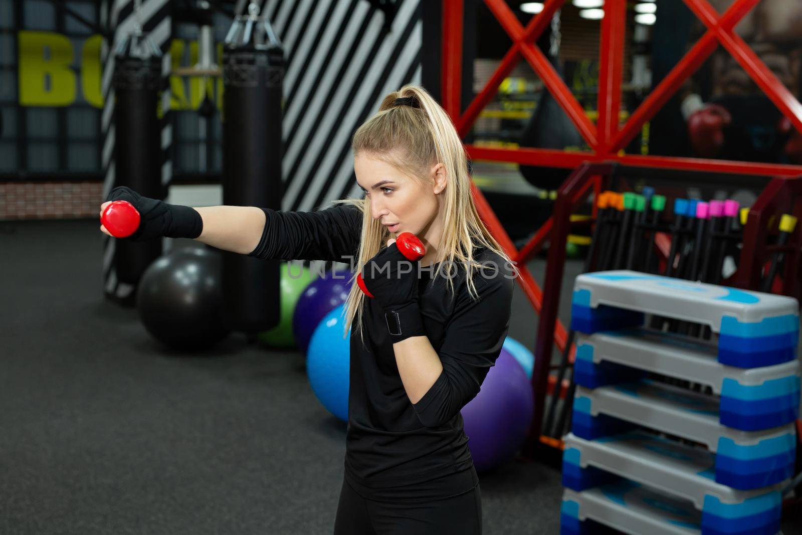 Cheerful sporty woman exercising hand punch with dumbbells in boxing ring