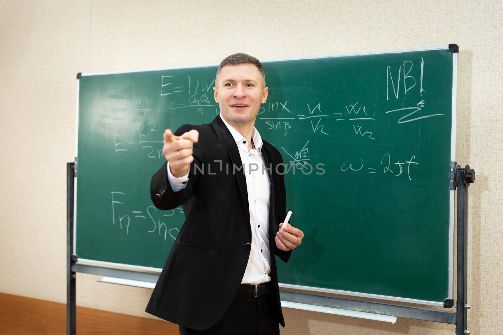 The male teacher used white chalk to write on the blackboard to teach students in a class by StudioPeace