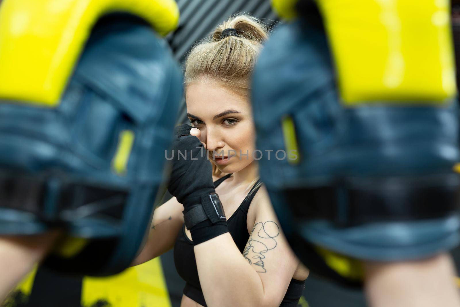 Beautiful girl in boxing gloves hits the paws held by her trainer.
