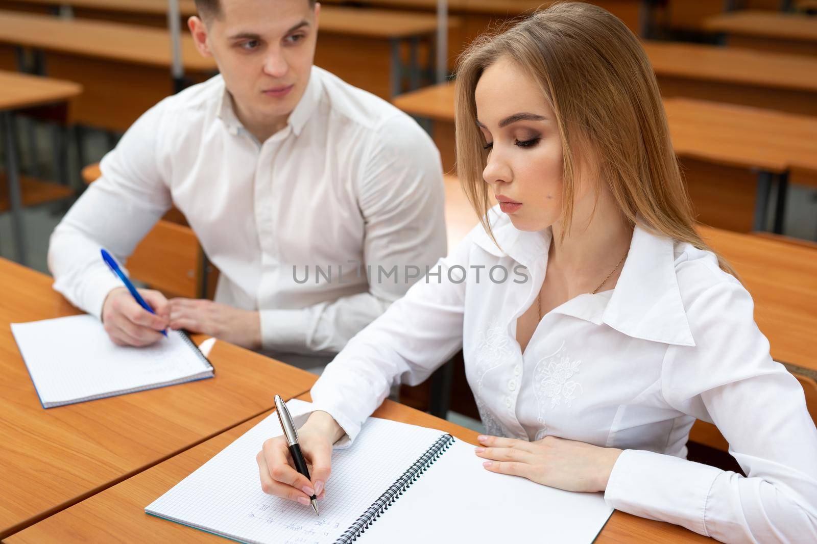 Young couple of students, a guy and a girl, sit at a desk at a lecture and hold hands.