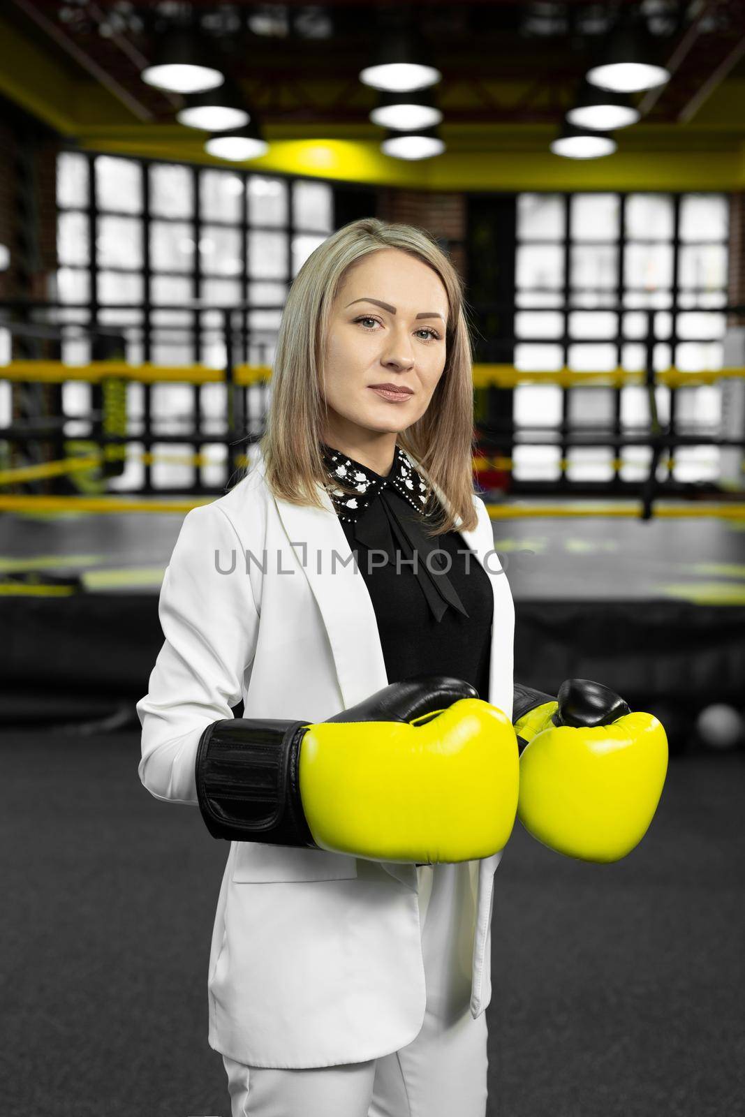 Portrait of a business woman in yellow boxing gloves on the background of a boxing ring. by StudioPeace