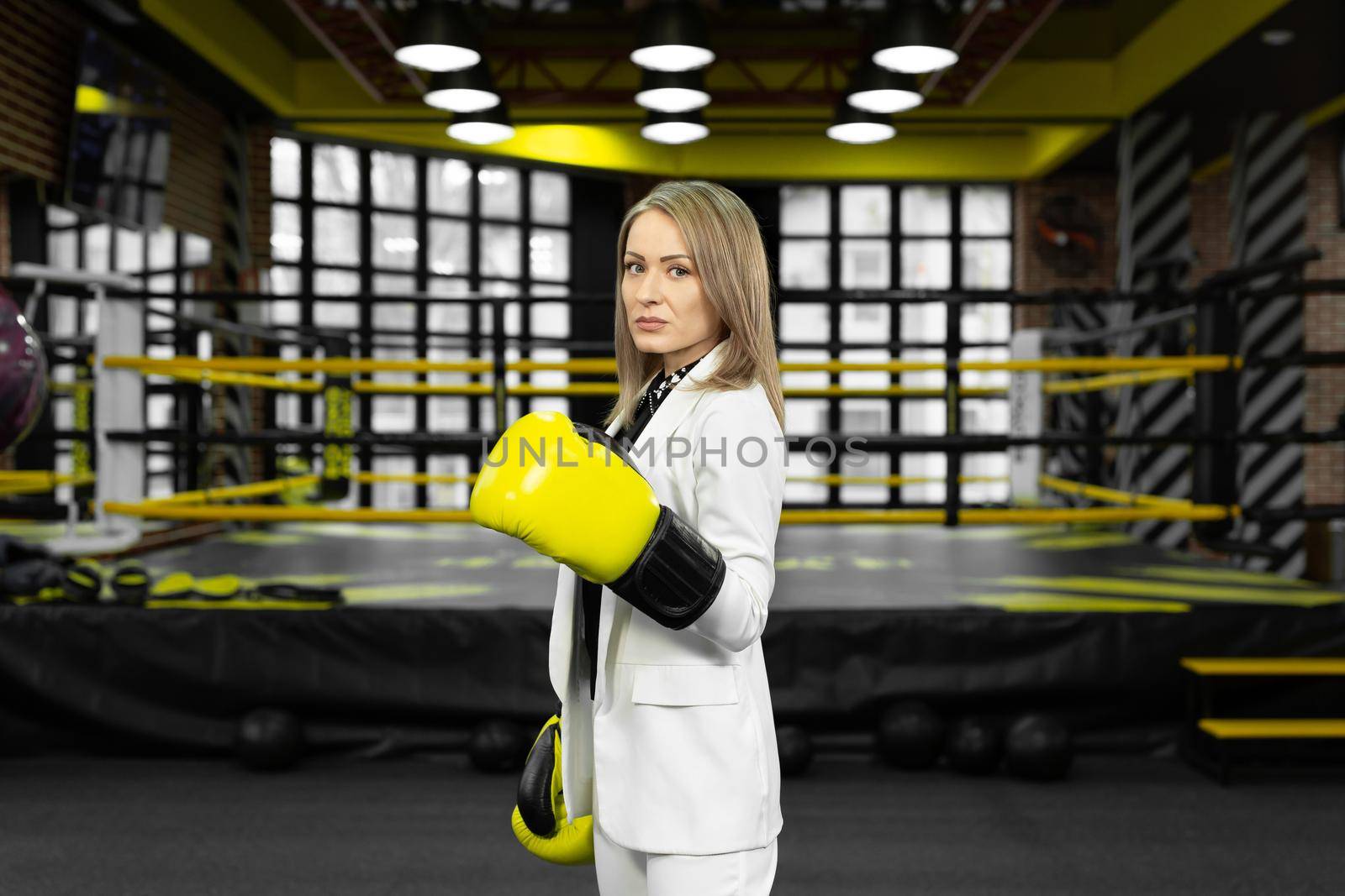 Portrait of a business woman in yellow boxing gloves on the background of a boxing ring. by StudioPeace