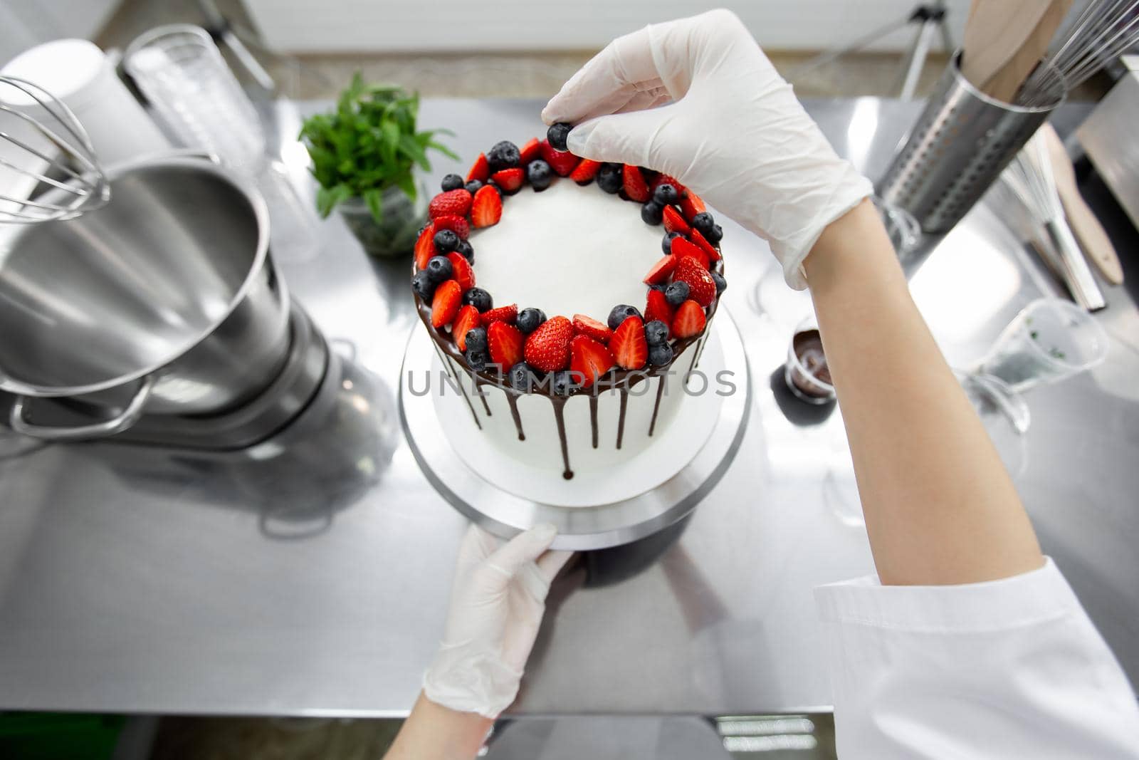 Pastry chef decorates the cake with chocolate streaks of strawberries and blueberries.