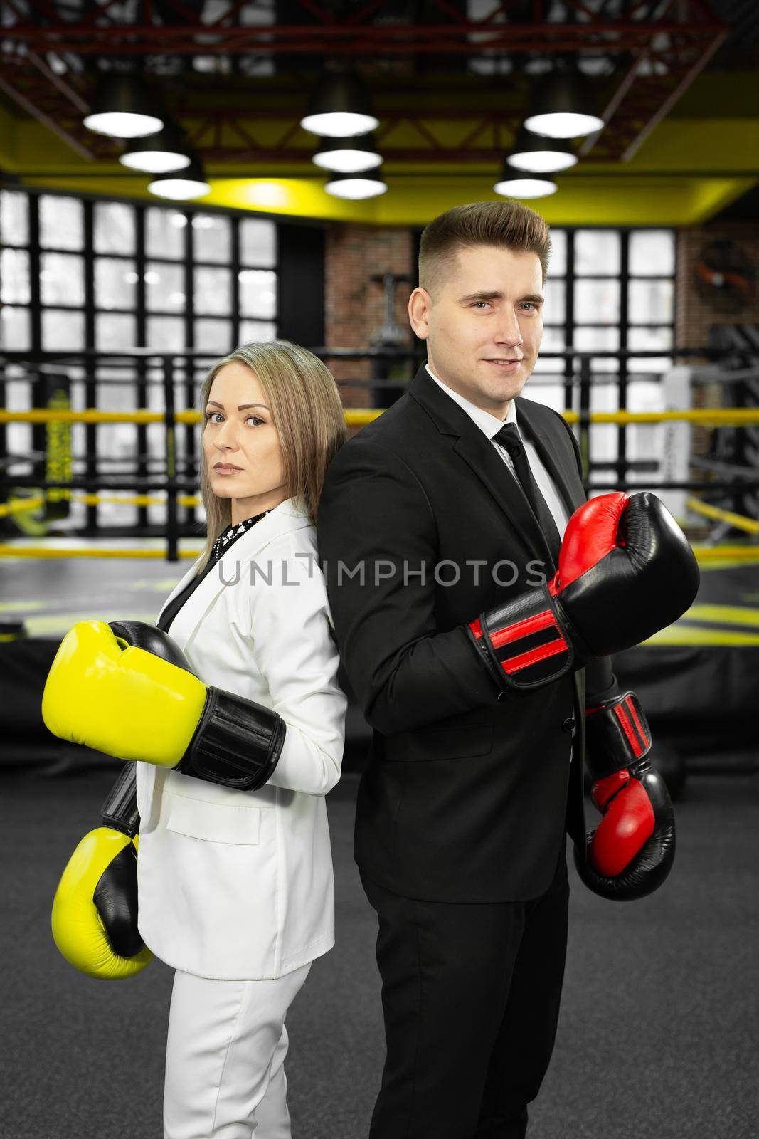 Man and woman in a suit and boxing gloves stand in front of the ring with their backs to each other by StudioPeace