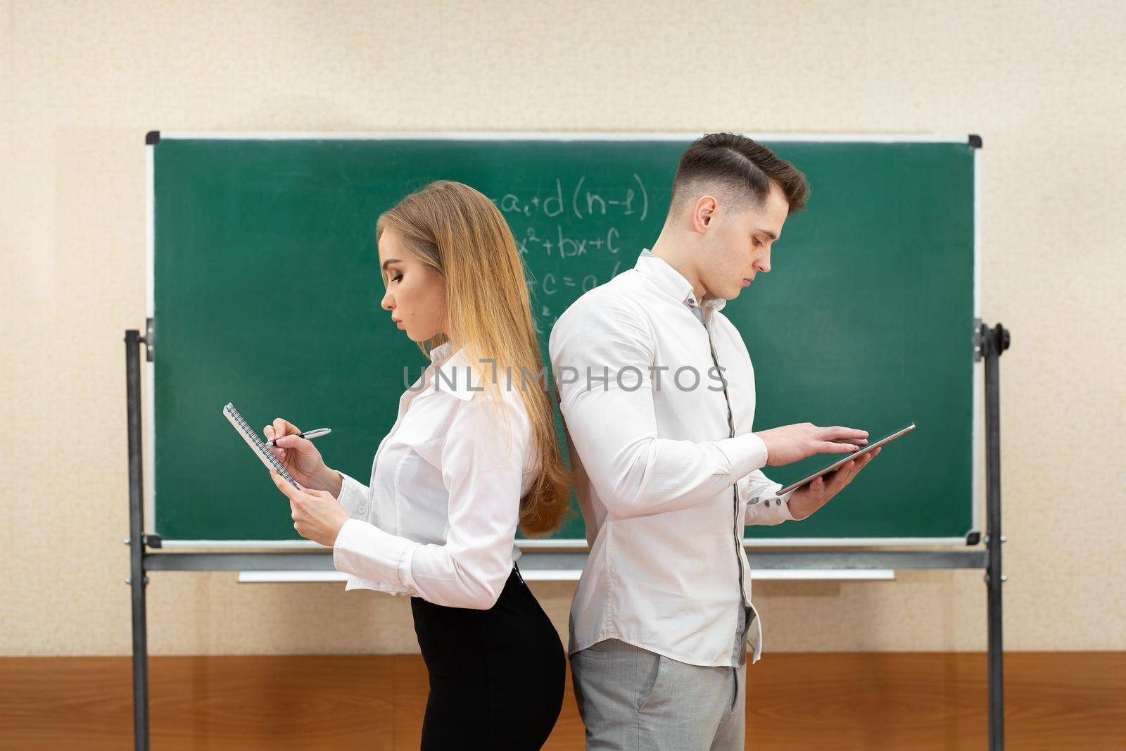 University students a guy and a girl pose with tablets in their hands near the blackboard.