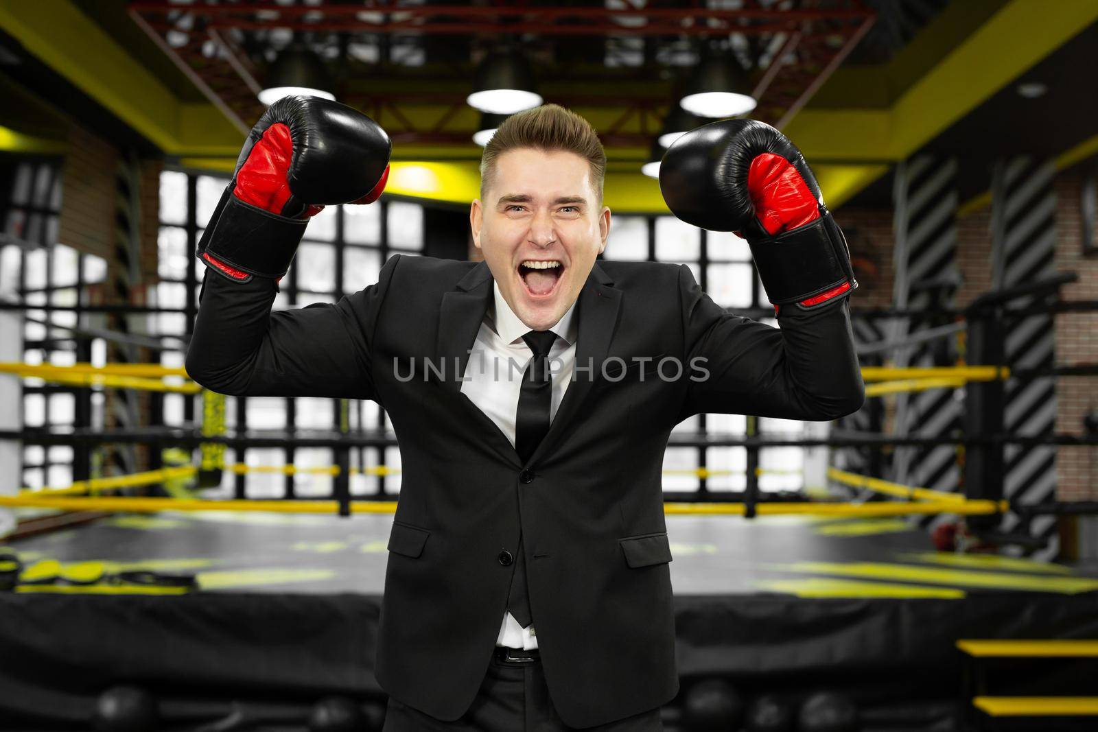 Young male businessman in a suit and boxing gloves is having fun and laughing.