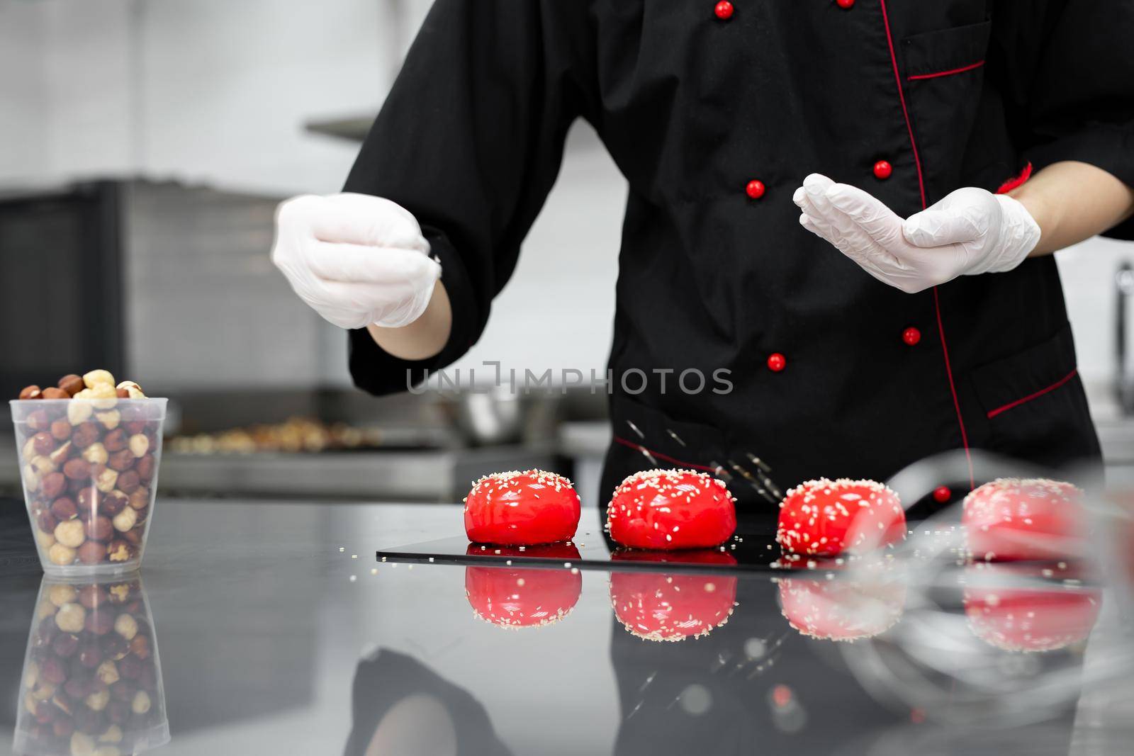 The pastry chef sprinkles the red mousse cake with sesame seeds.