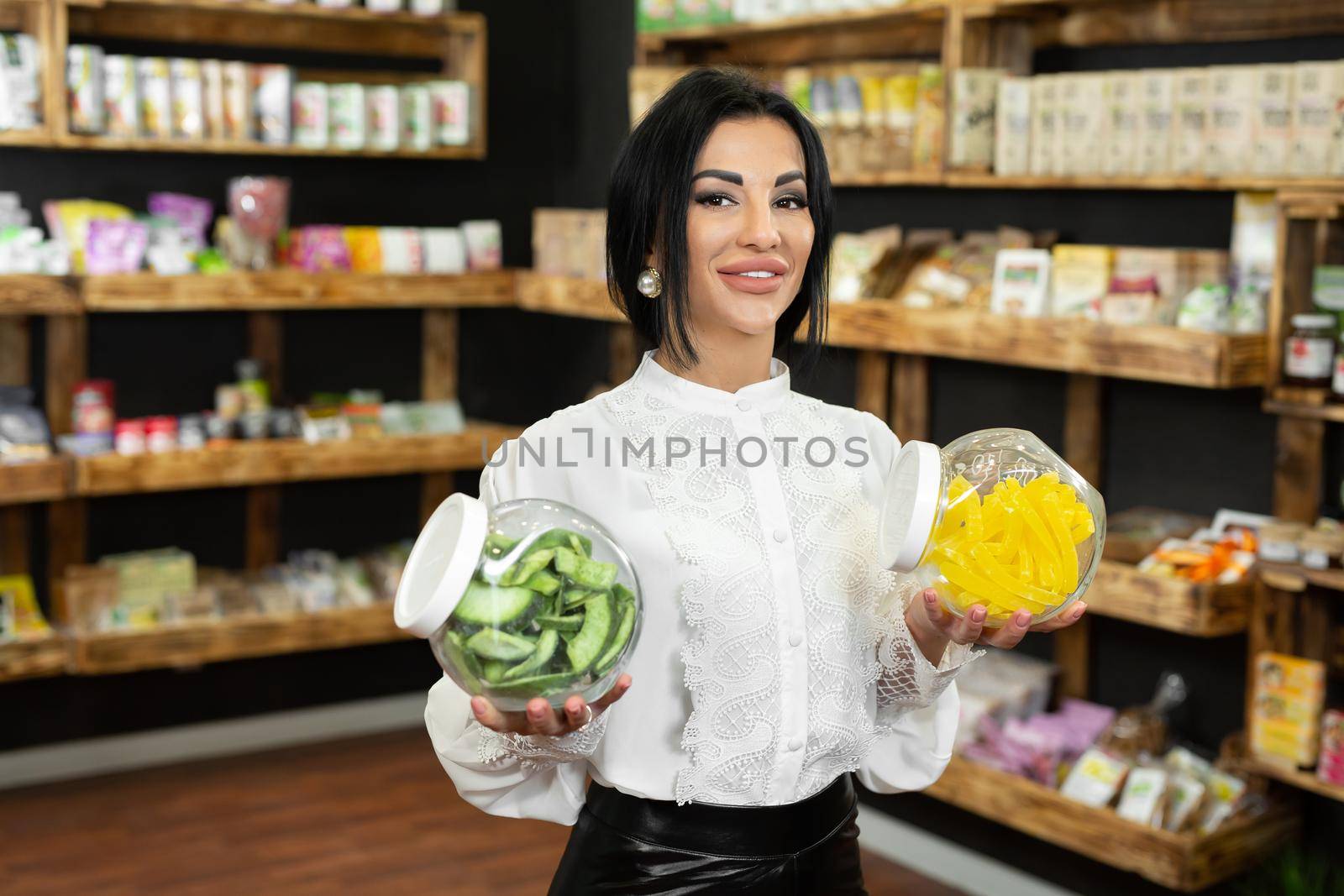 Glass jars with dried fruits and candied fruits in the hands of a female saleswoman in a health food store.