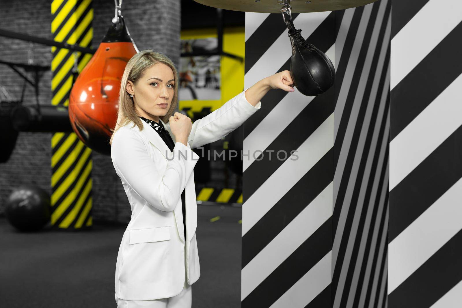 Serious, focused businesswoman hits a punching bag in the gym. The concept of anger management.