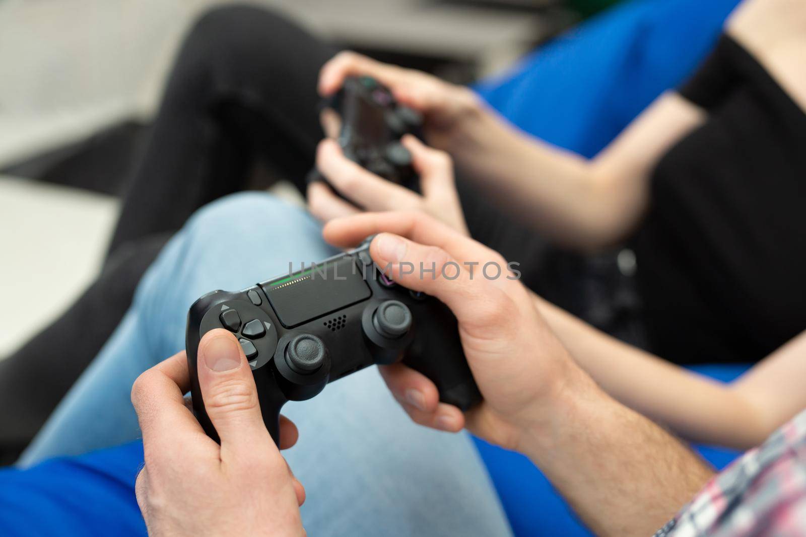 Close-up of the hands of a man and a woman enjoying playing video games with a console gamepad in their hands by StudioPeace