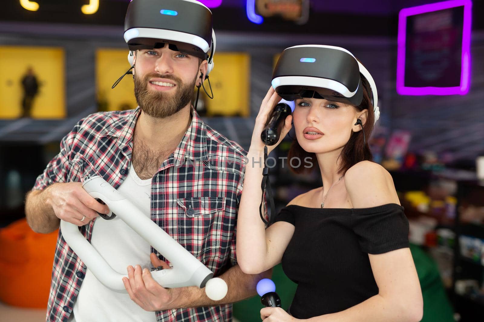 Portrait of a man and a woman with a virtual reality headset with glasses and hand motion controllers in a game club.