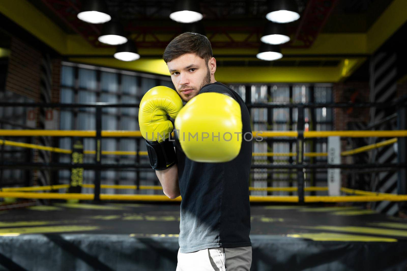 The assembled athlete in the boxing gym practices boxing punches during training and looks at the camera. by StudioPeace