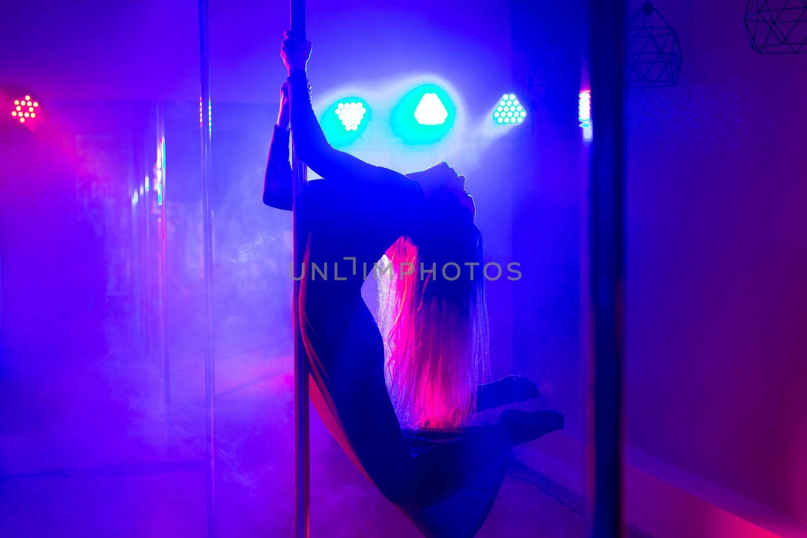 Pole dance. Young slender sexy woman dancing on a pole in the interior of a nightclub with light and smoke by StudioPeace