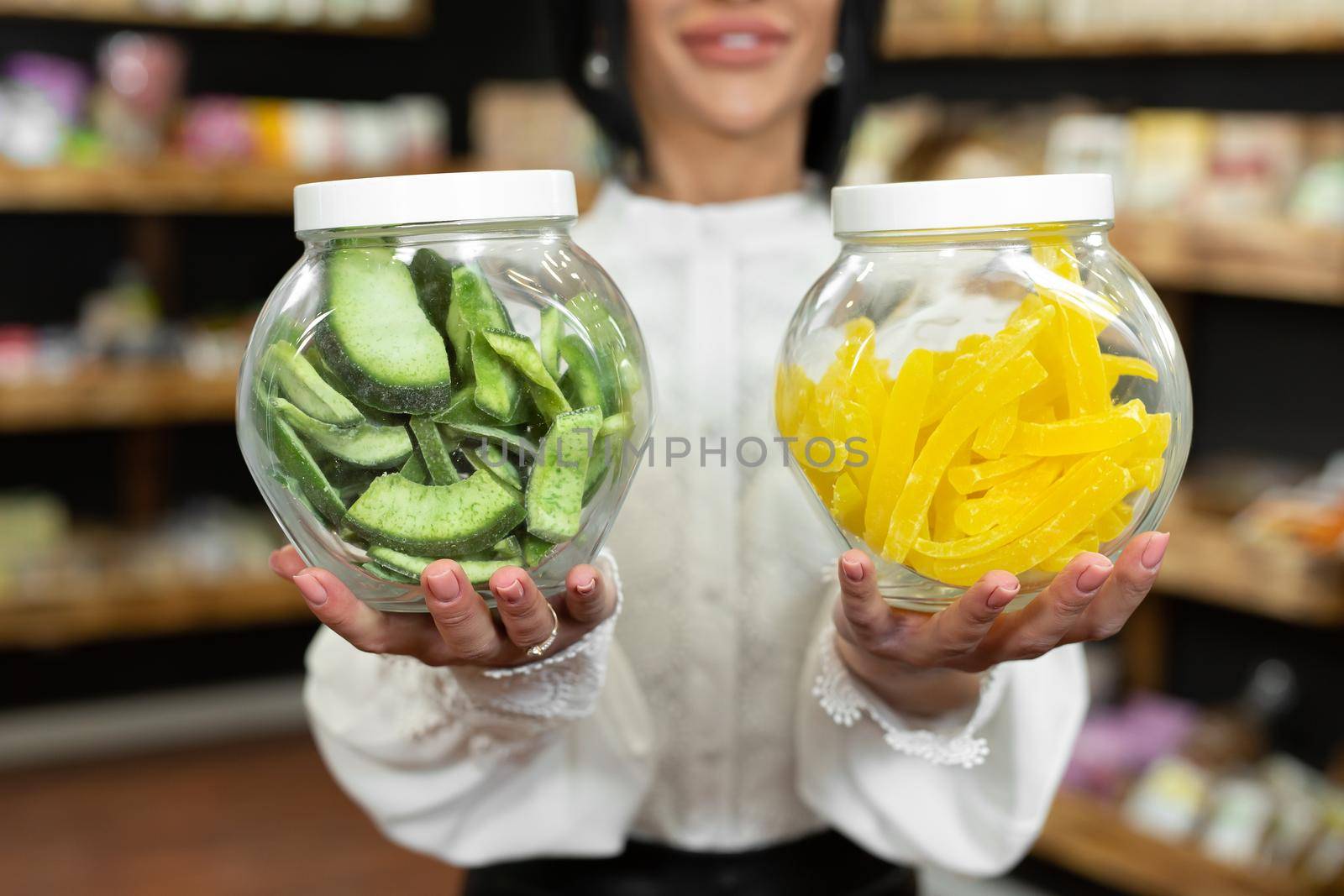 Glass jars with dried fruits and candied fruits in the hands of a female saleswoman in a health food store.