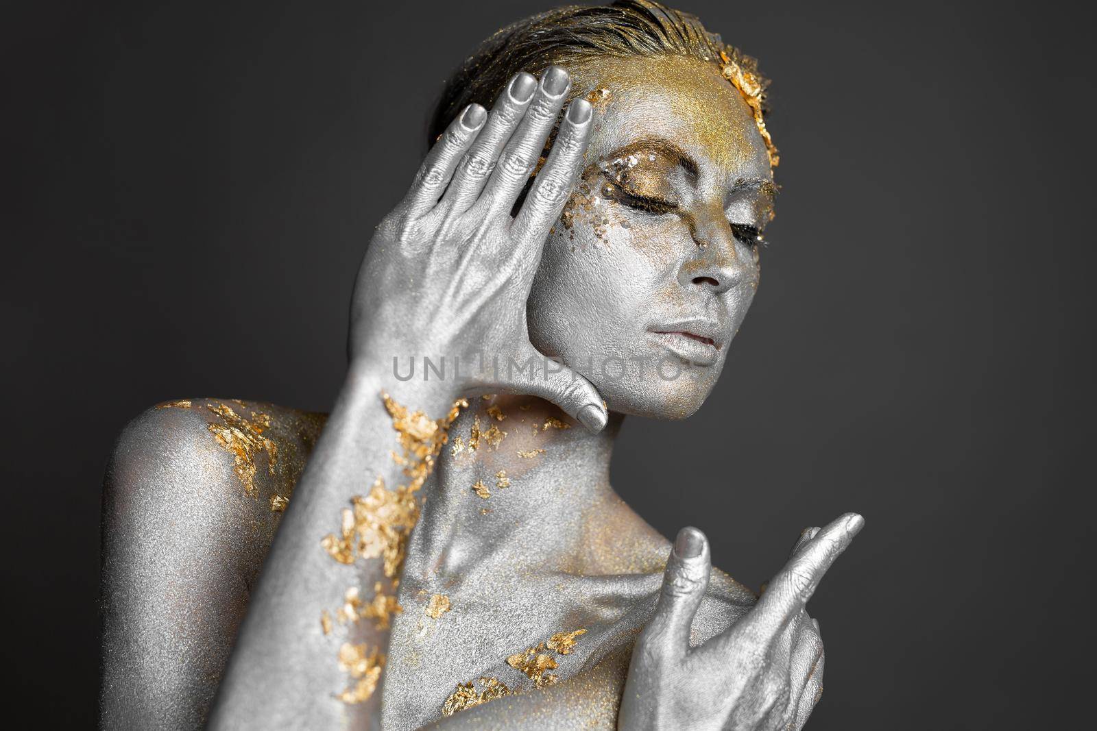 Portrait of a beautiful female model with gold and silver paint on her skin and hair in the studio.