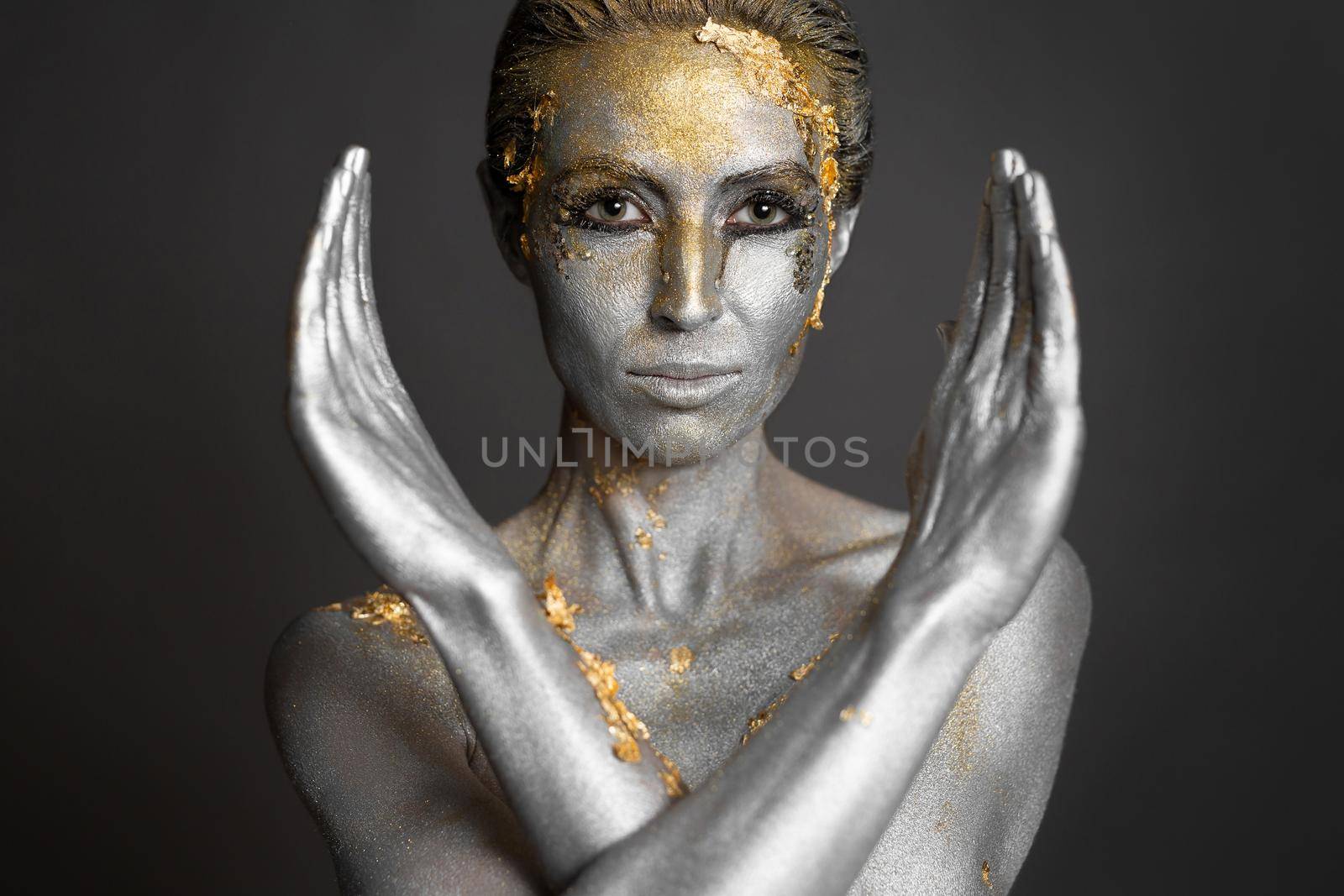 Portrait of a beautiful female model with gold and silver paint on her skin and hair in the studio.