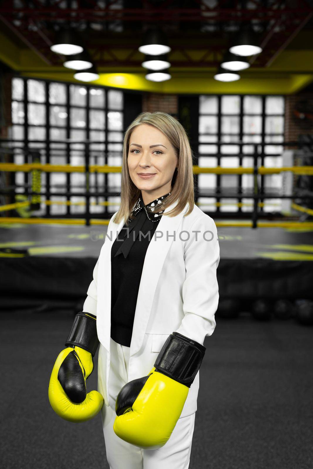 Portrait of a business woman in yellow boxing gloves on the background of a boxing ring