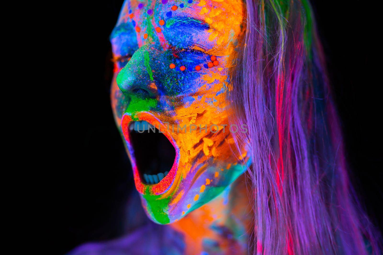 Beautiful young woman in neon light. Portrait of a model with fluorescent makeup who poses in UV light and screams