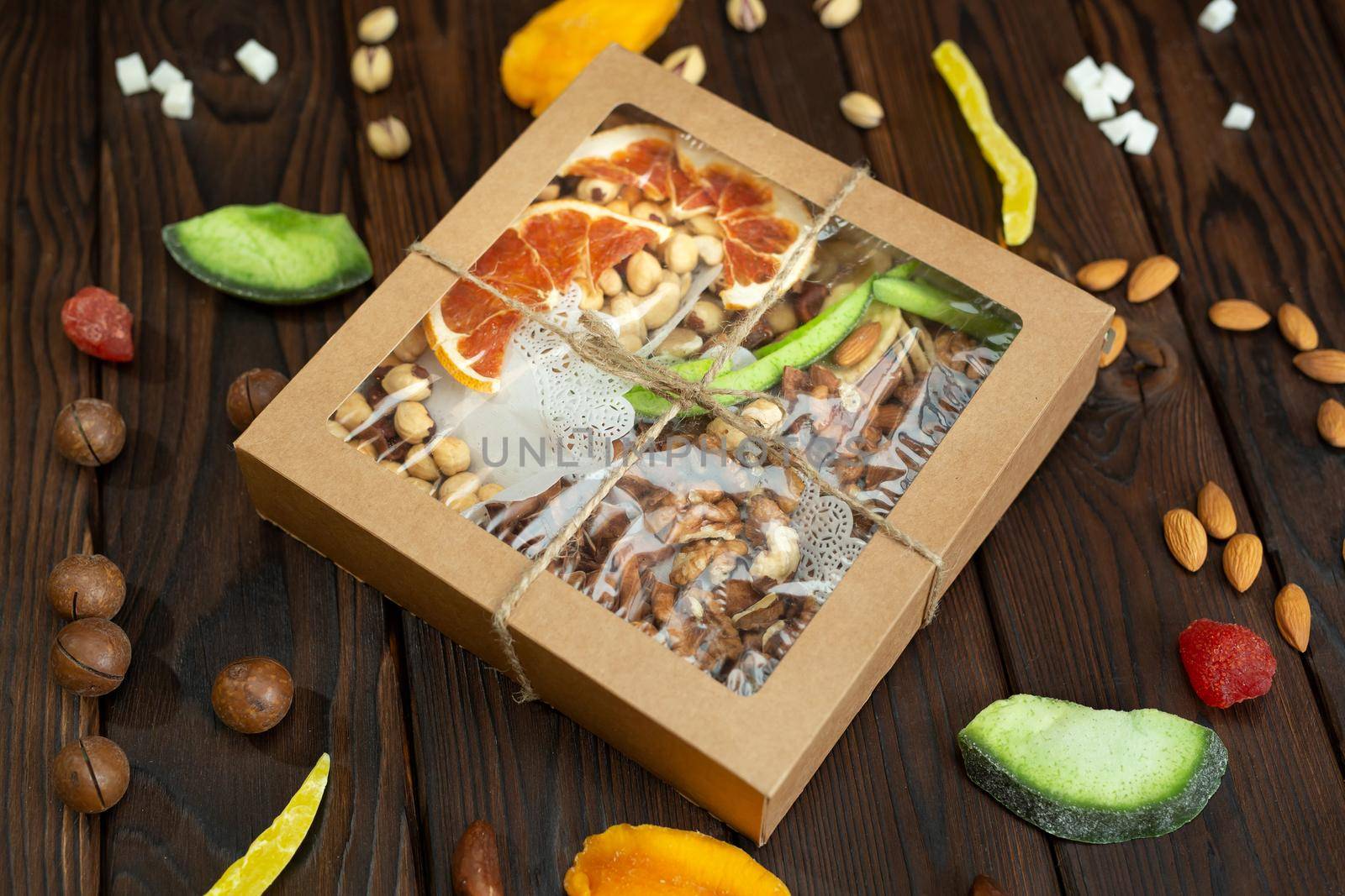 Nuts, candied fruits and dried fruits of different varieties in a paper box on a structural wooden background top view.