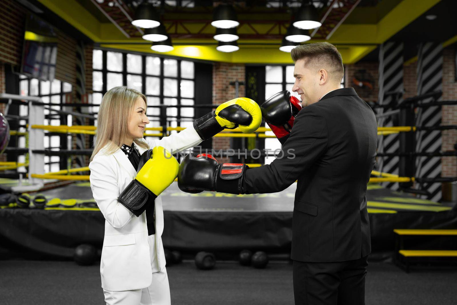 Picture of a businessman and a businesswoman sparring with boxing gloves against of a boxing ring.