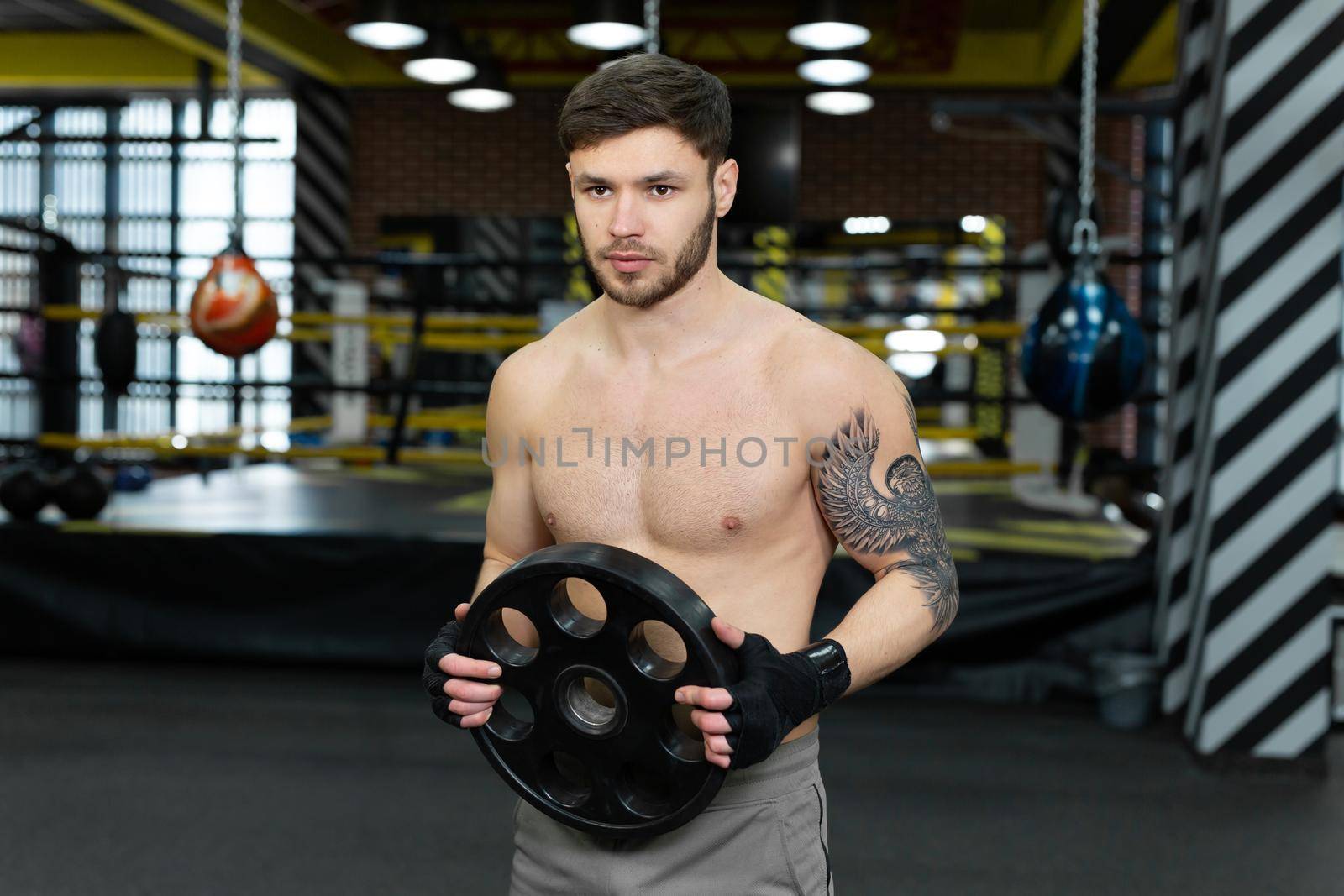 Young muscular guy with a naked torso posing holding a pancake from a barbell