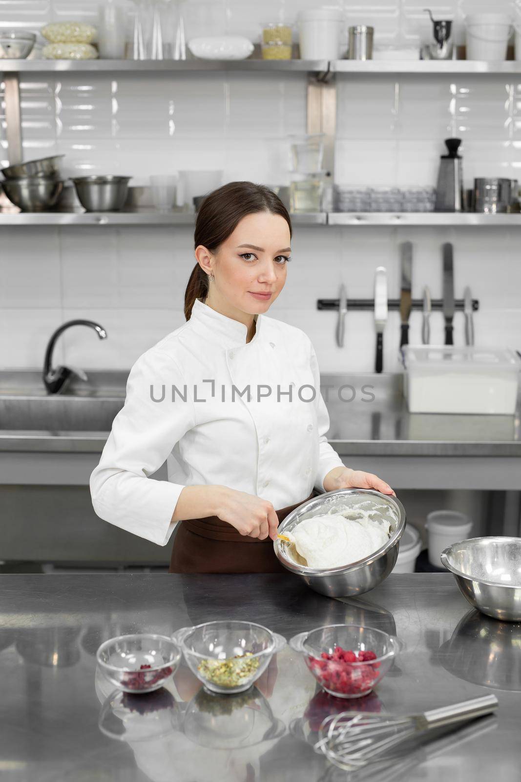 Young cute female baker mixes dough in a large bowl and smiles. The process of making a cake or cupcakes. by StudioPeace