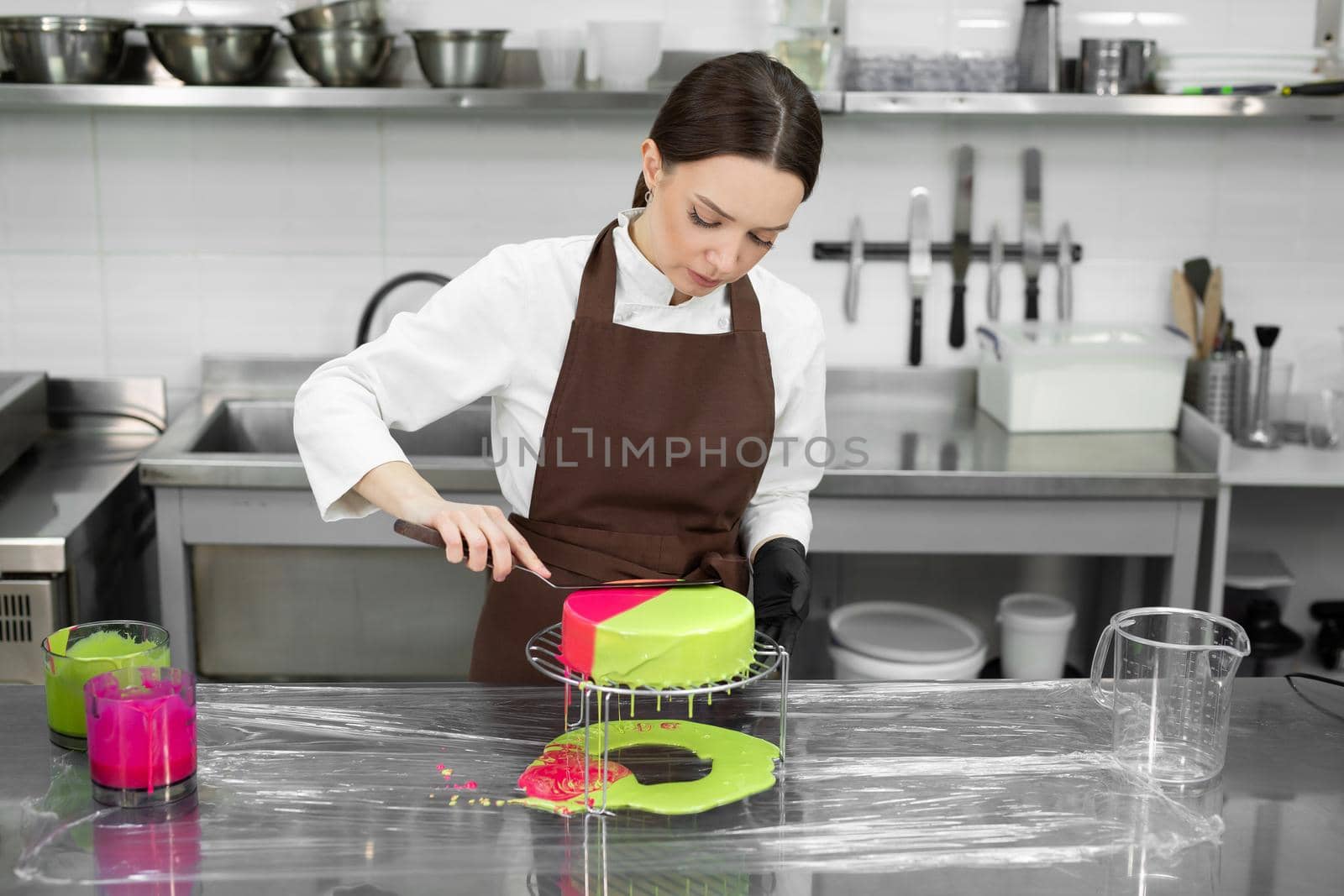 Female pastry chef decorates a mousse cake with a mirror glaze.