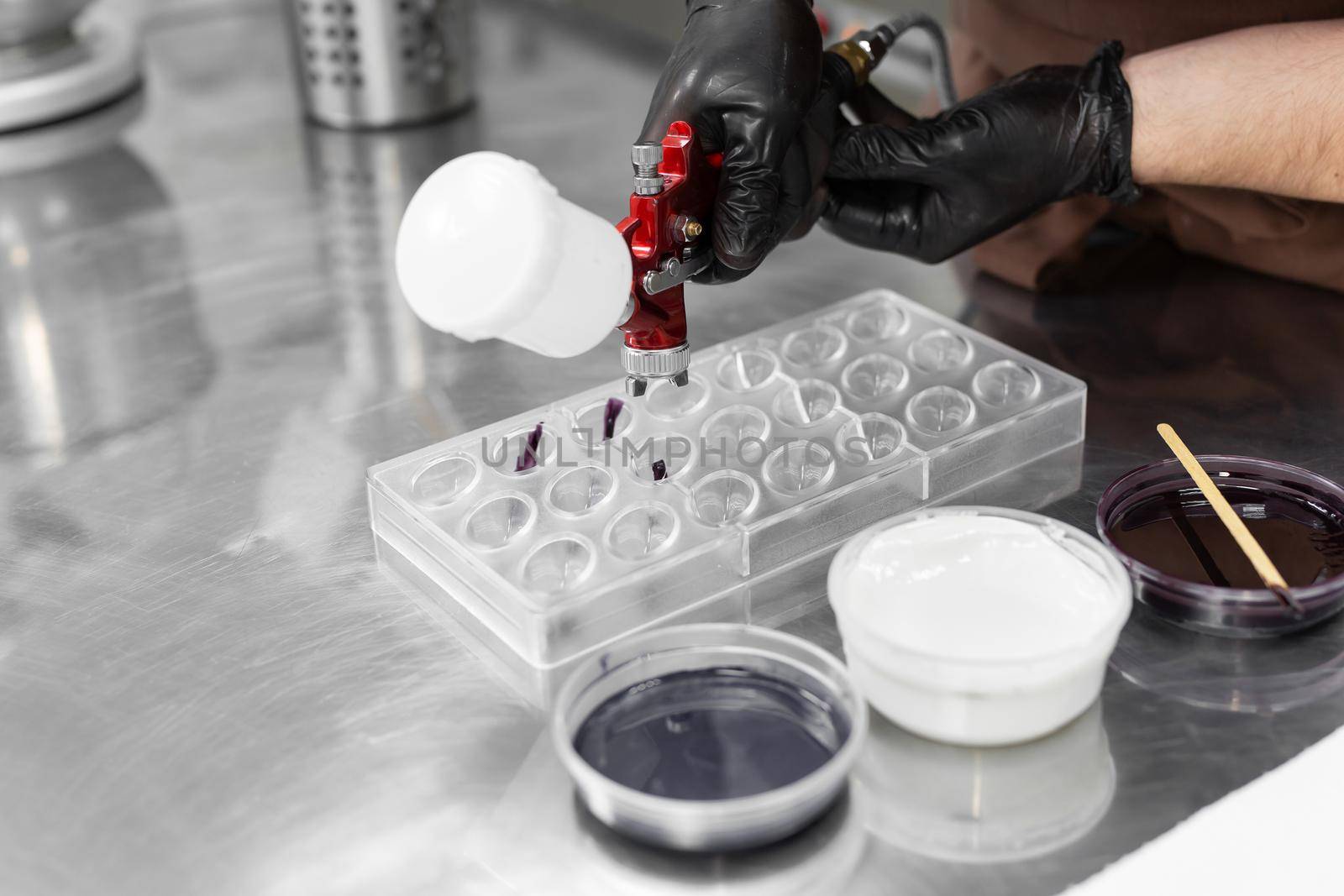 Close-up of the hands of a male pastry chef who sprays food paint with a pastry airbrush in the kitchen when making chocolates.