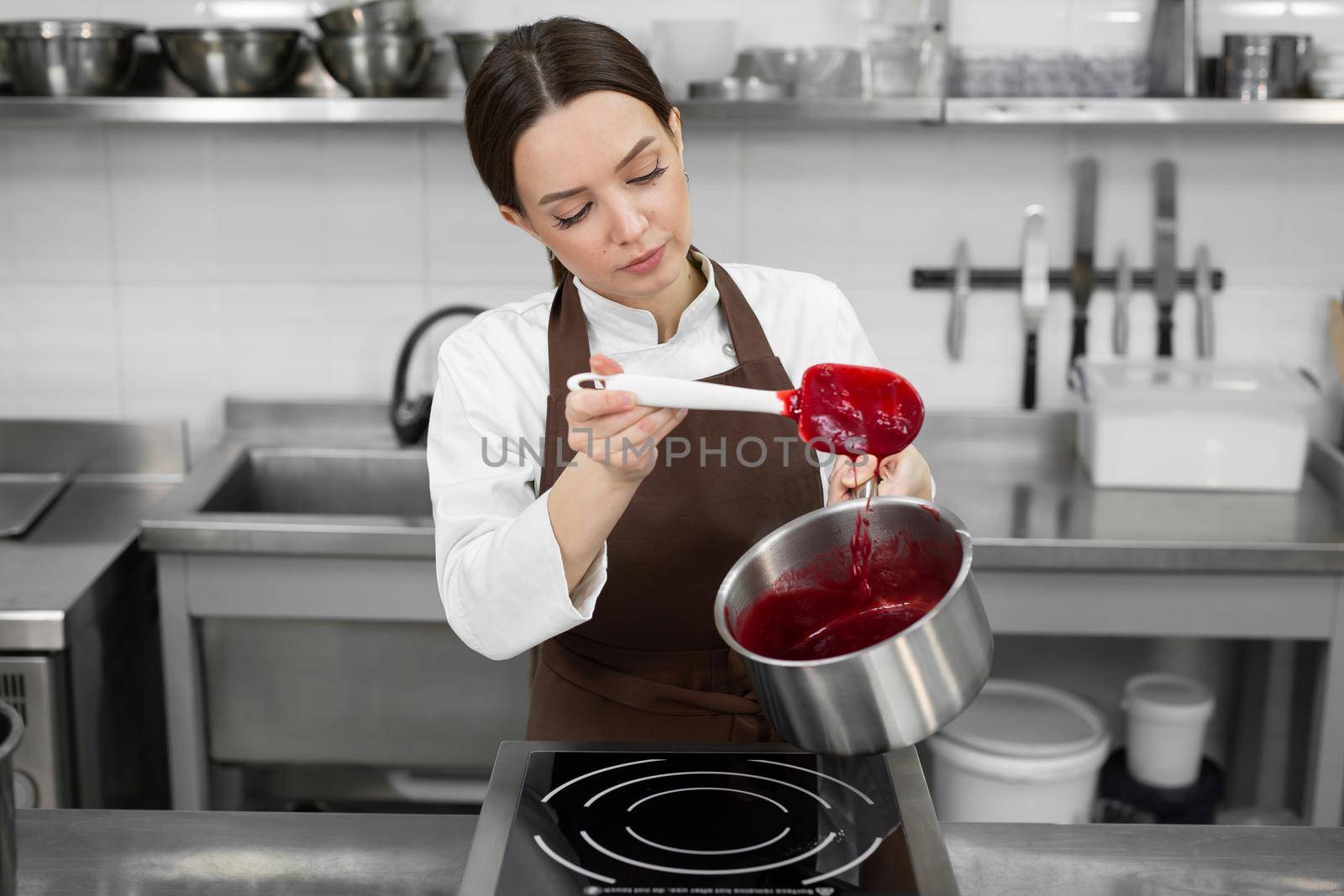 Female pastry chef prepares berry confit in a pot for filling a cake in a professional kitchen.